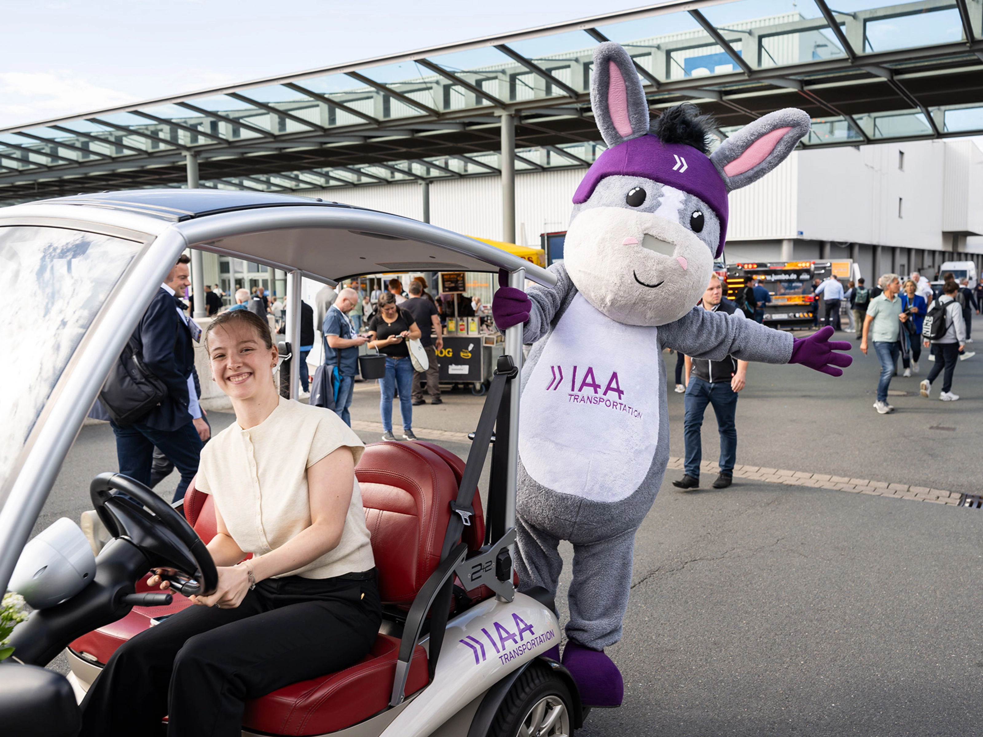 Frau in einem IAA-Fahrzeug neben dem IAA Transportation Maskottchen auf der Messe.