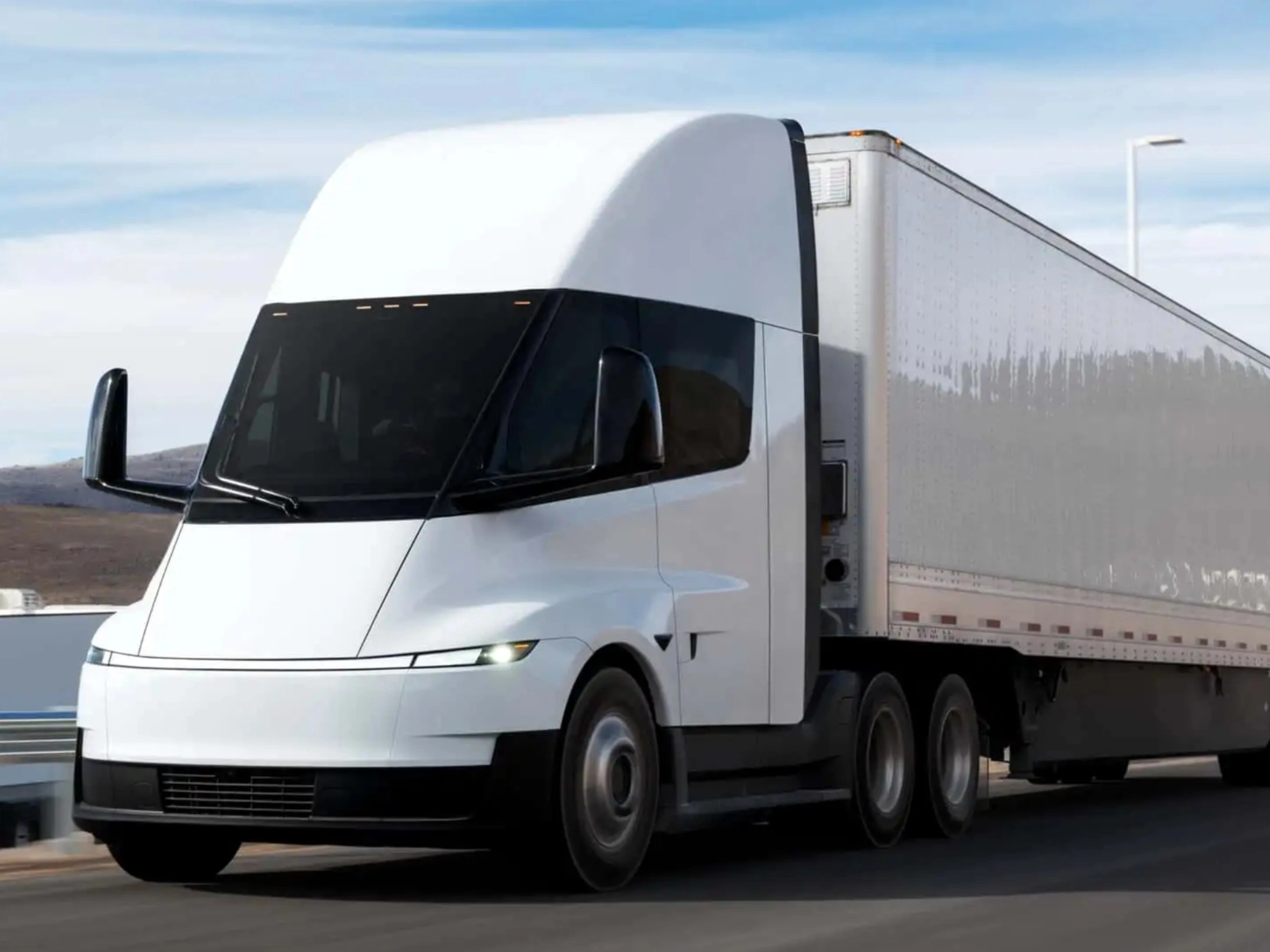 Electric semi-truck driving on a highway in a rural landscape.
