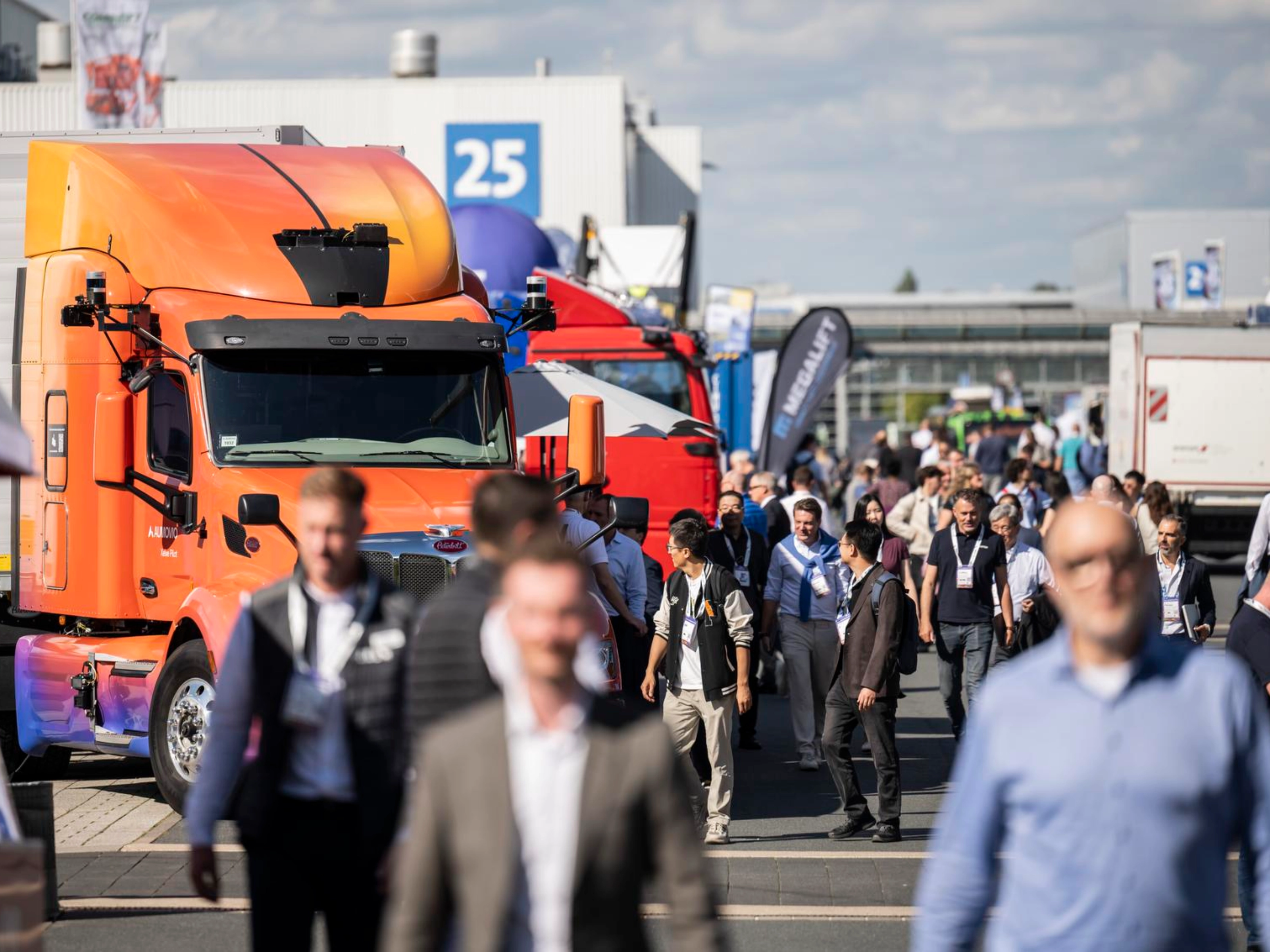 Besucher gehen auf einem belebten Messegelände zwischen Lkw hindurch.