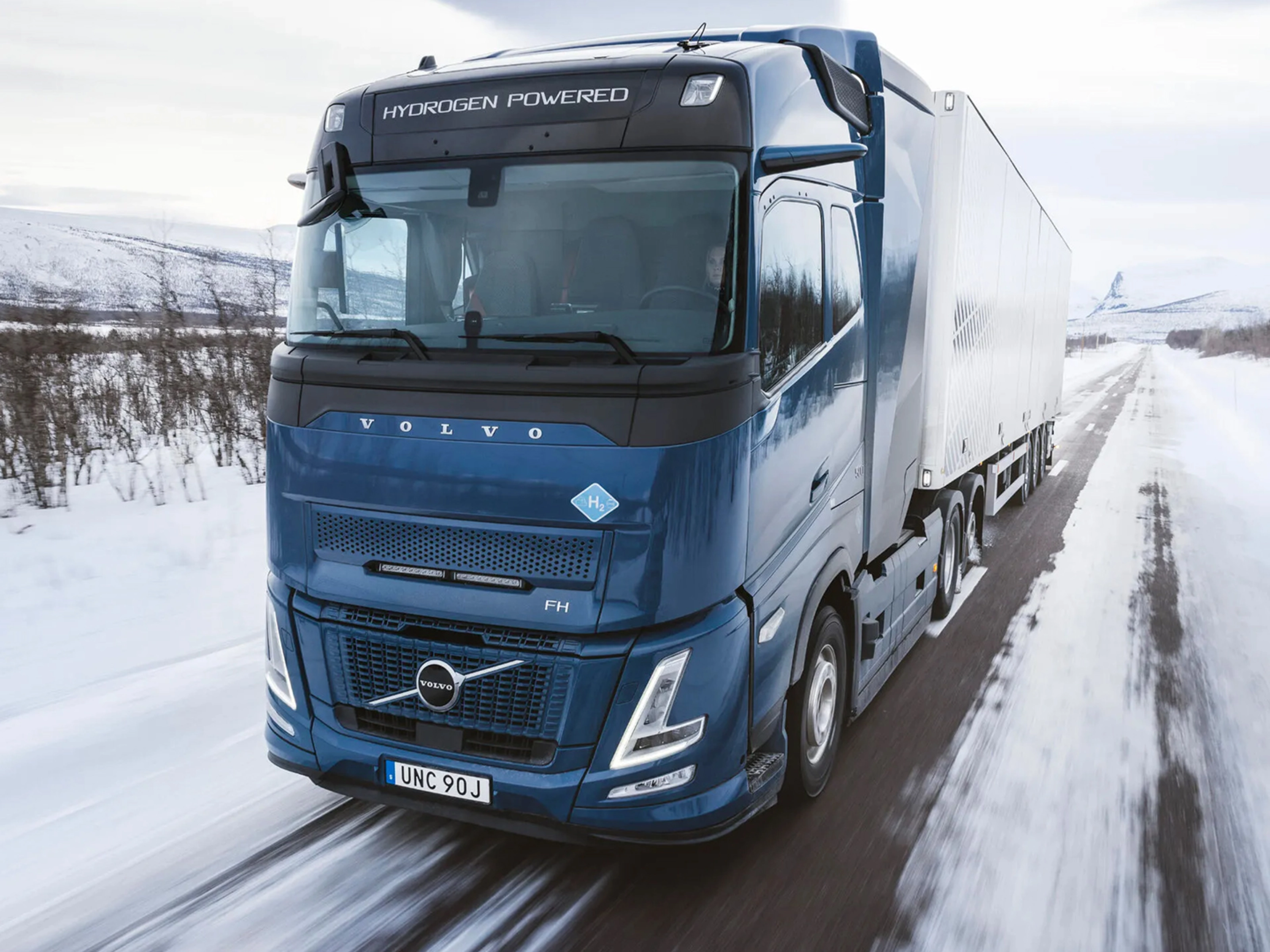 Wasserstoffbetriebener Volvo-Lkw fährt auf verschneiter Straße durch Winterlandschaft.