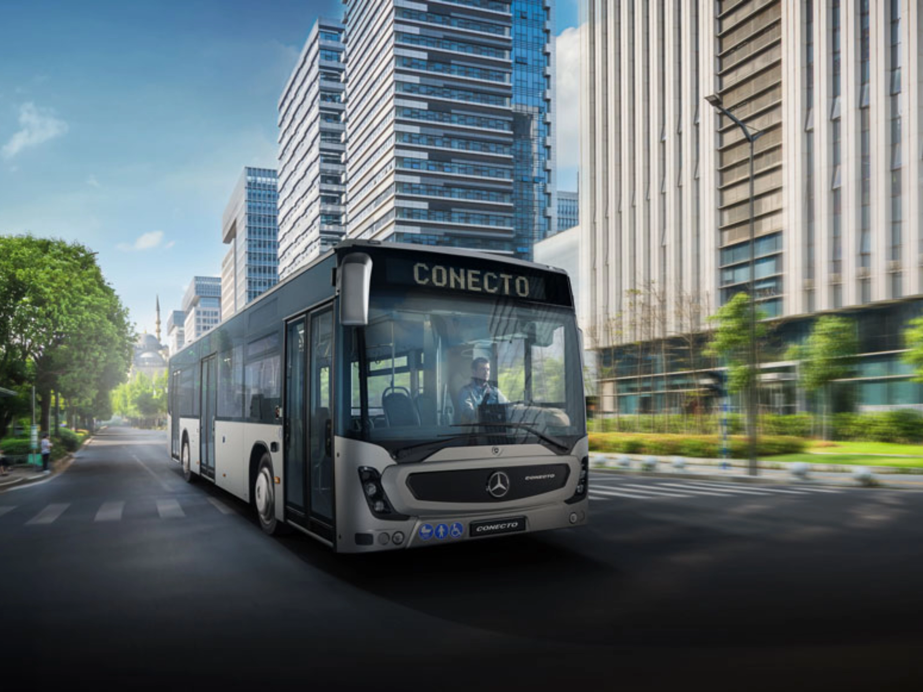 Modern city bus driving on a wide street between tall office buildings.