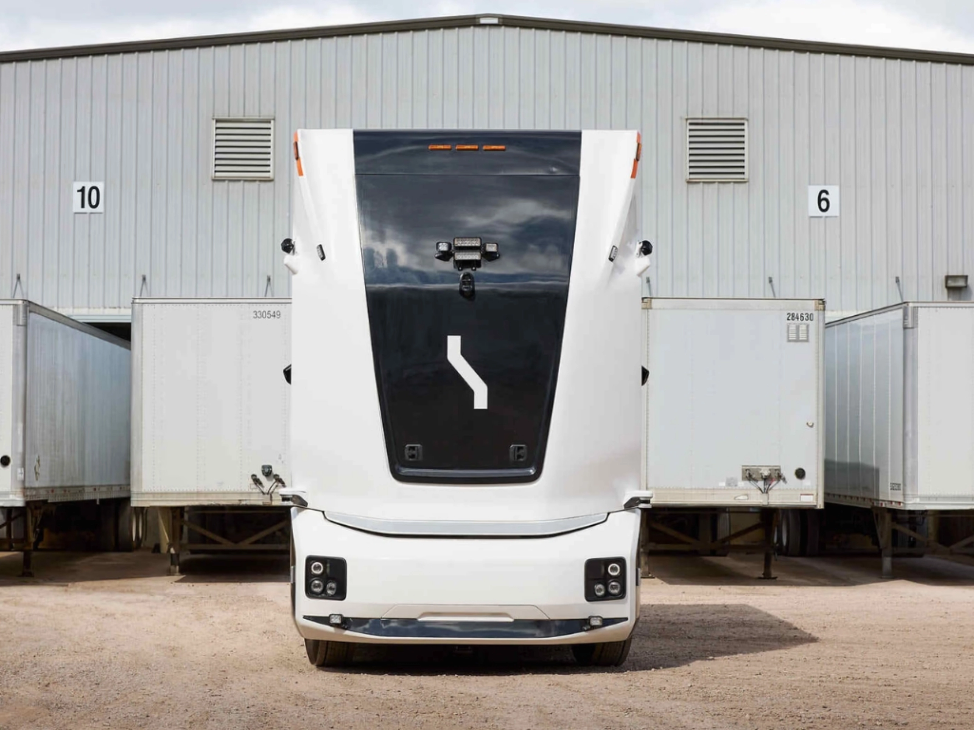 Einride autonomous electric truck in front of a warehouse with trailers.