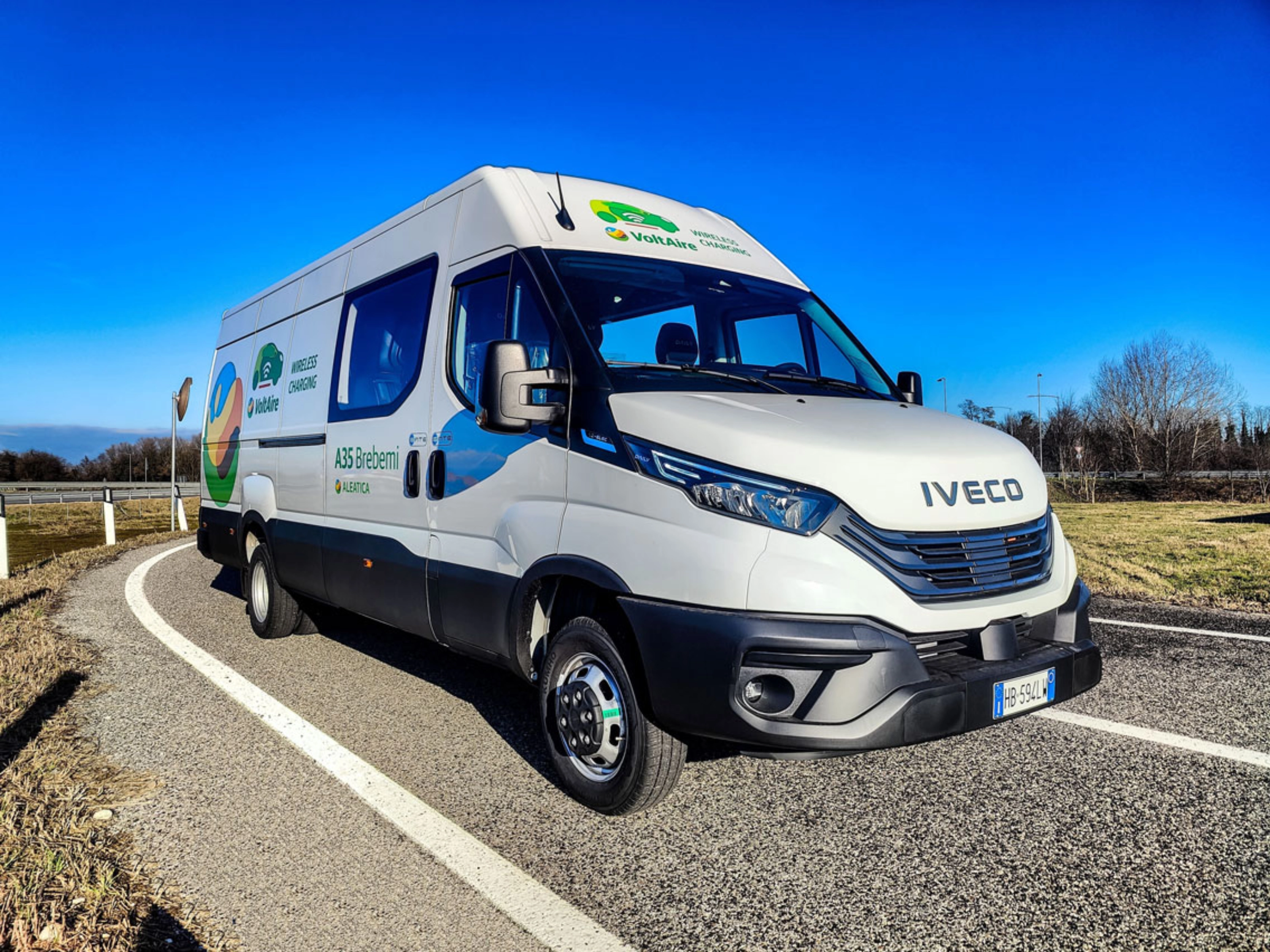 Ein weißer Iveco-Transporter fährt auf einer kurvigen Straße bei blauem Himmel.