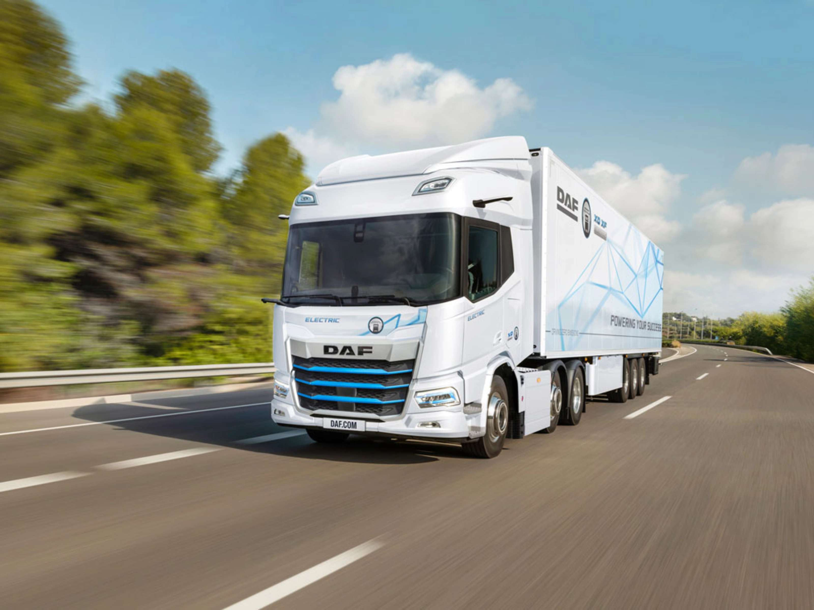 A white DAF electric truck is driving on a curved highway surrounded by greenery.