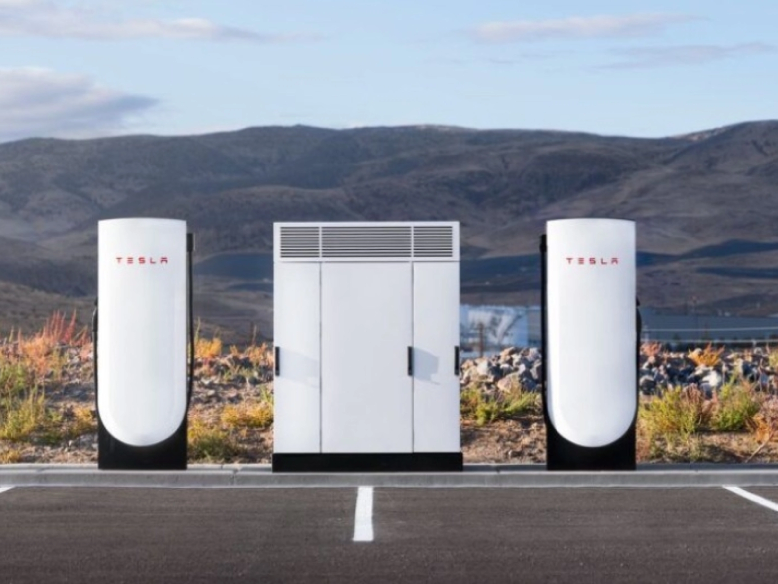 Tesla Supercharger station with two charging posts and a central power unit in a parking lot.