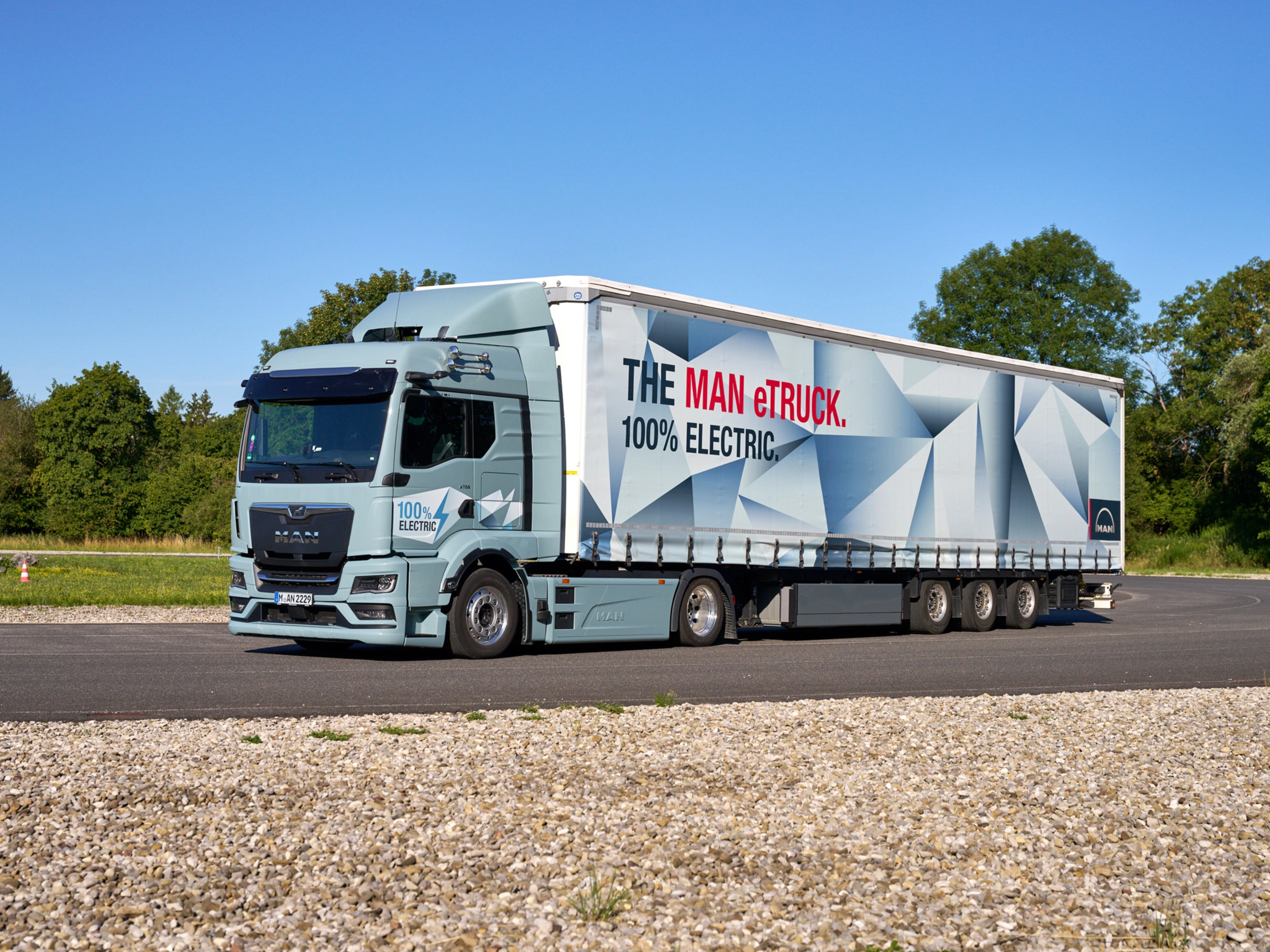 MAN truck with a trailer featuring a large graphic parked on a paved area.