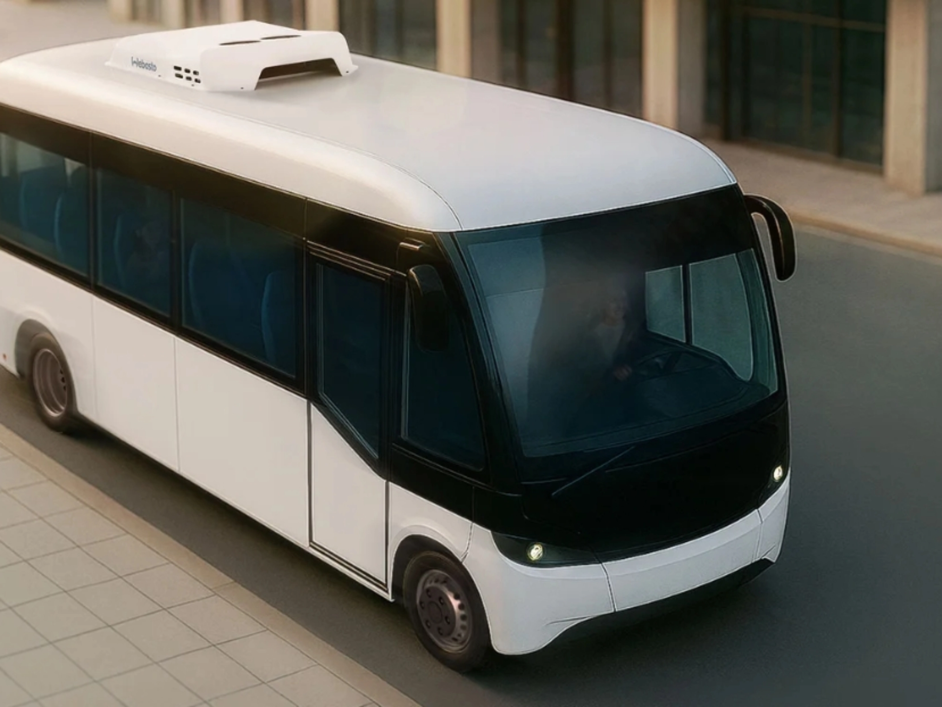 Small white autonomous shuttle bus driving on a city street, viewed from above.