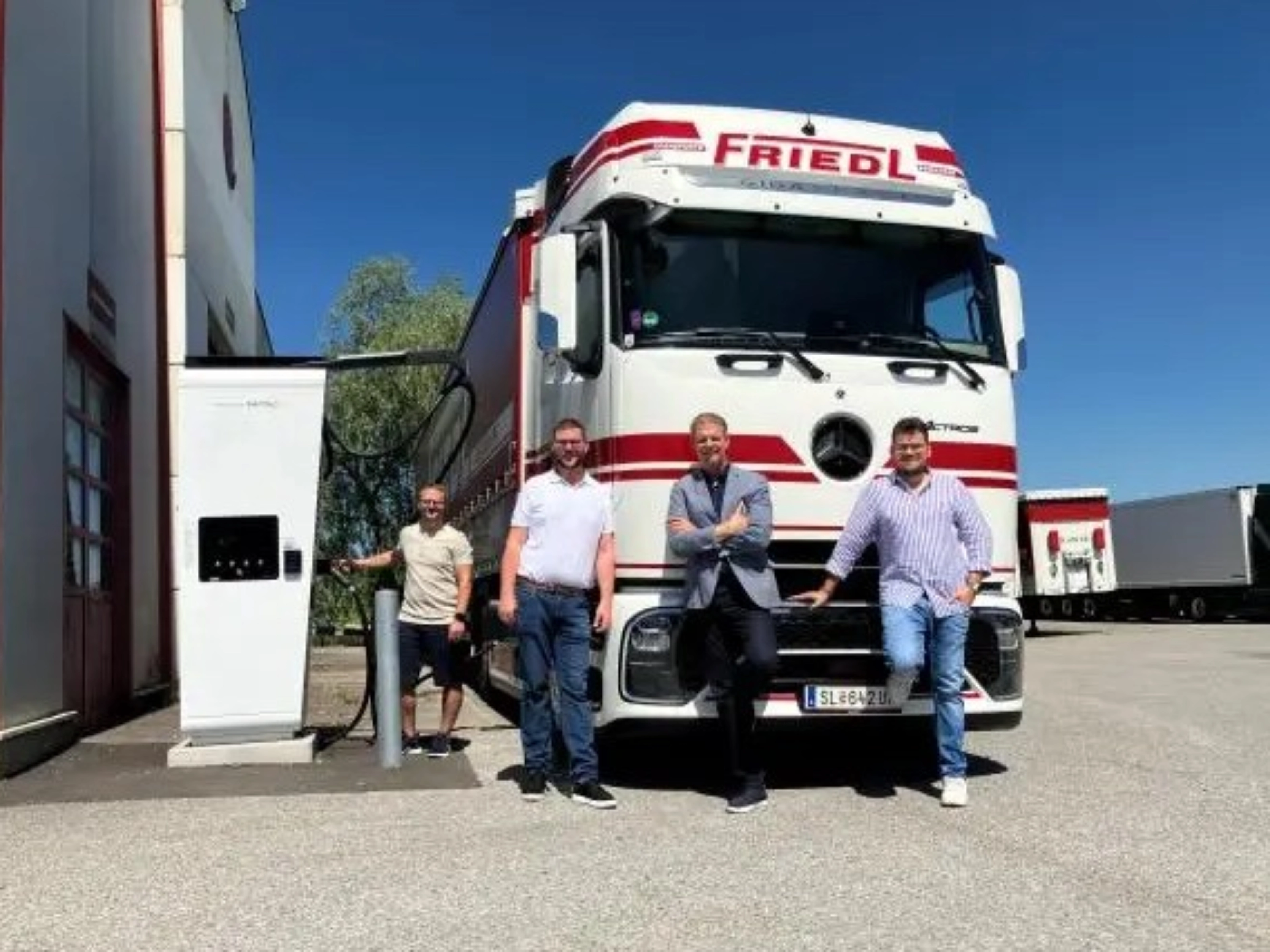 Vier Männer stehen vor einem weißen Frigel Lkw.