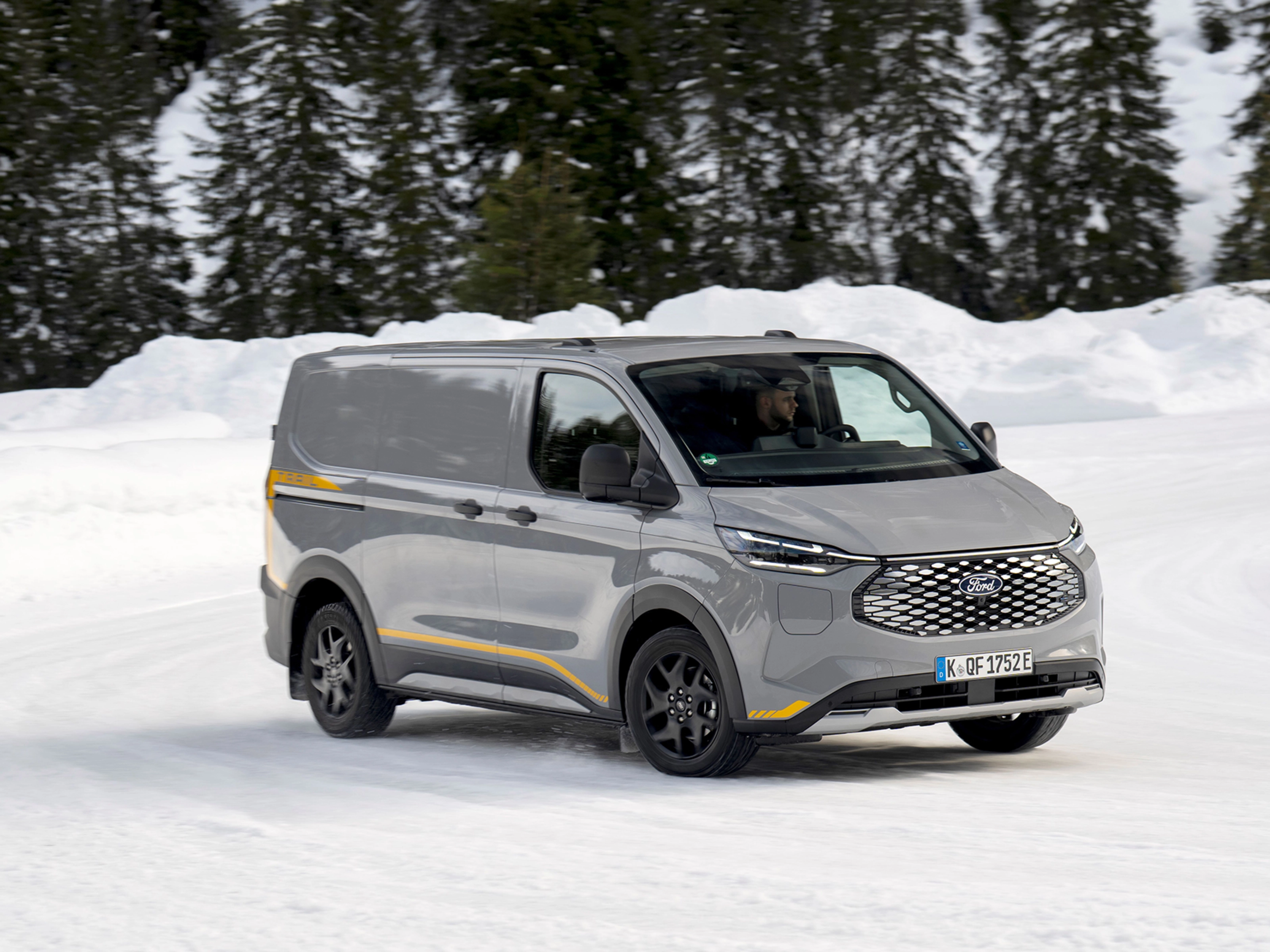 Grey Ford electric van driving on a snowy road with forest in the background.