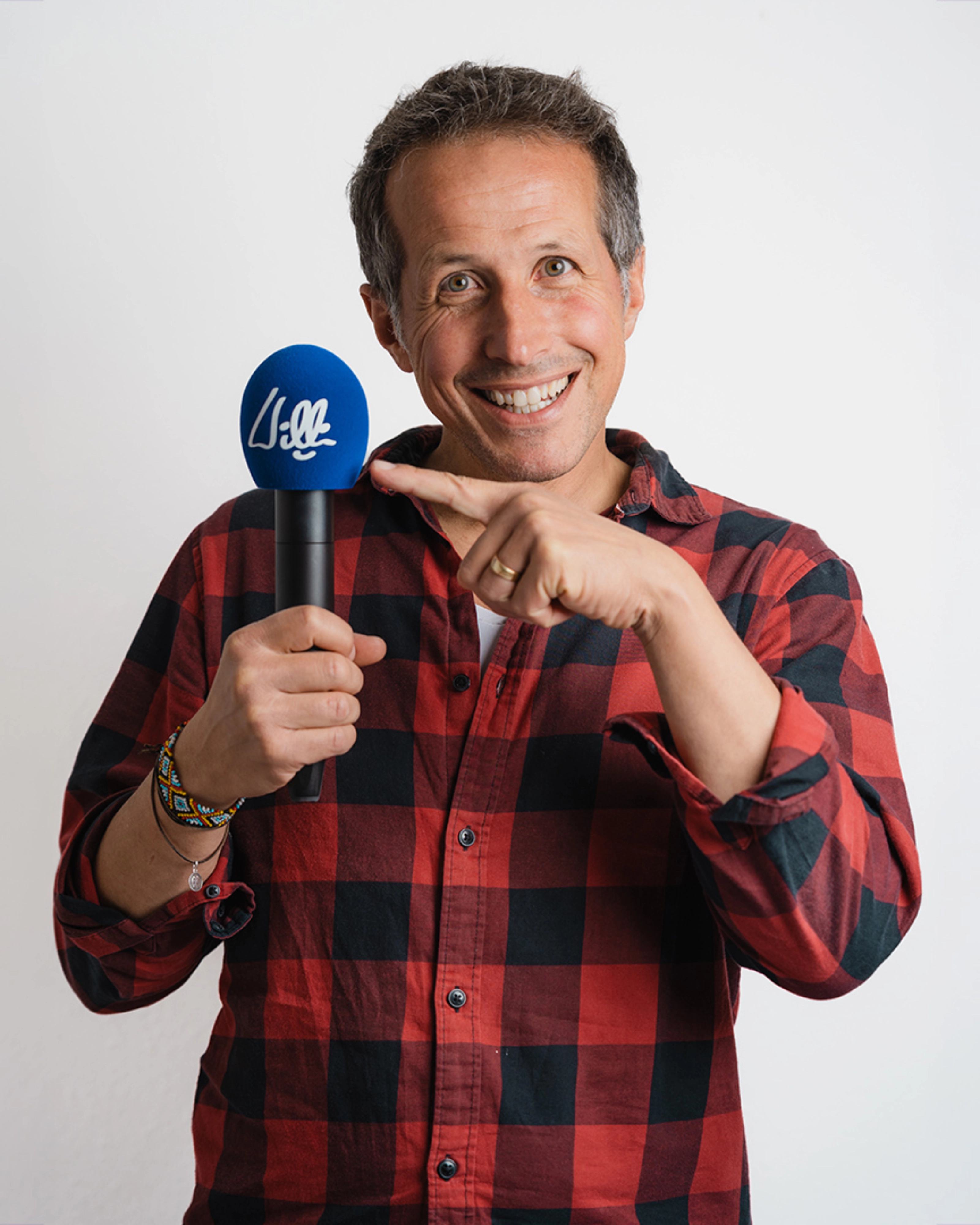 Willi Weitzel lächelt und zeigt in einem Porträt auf ein Mikrofon.