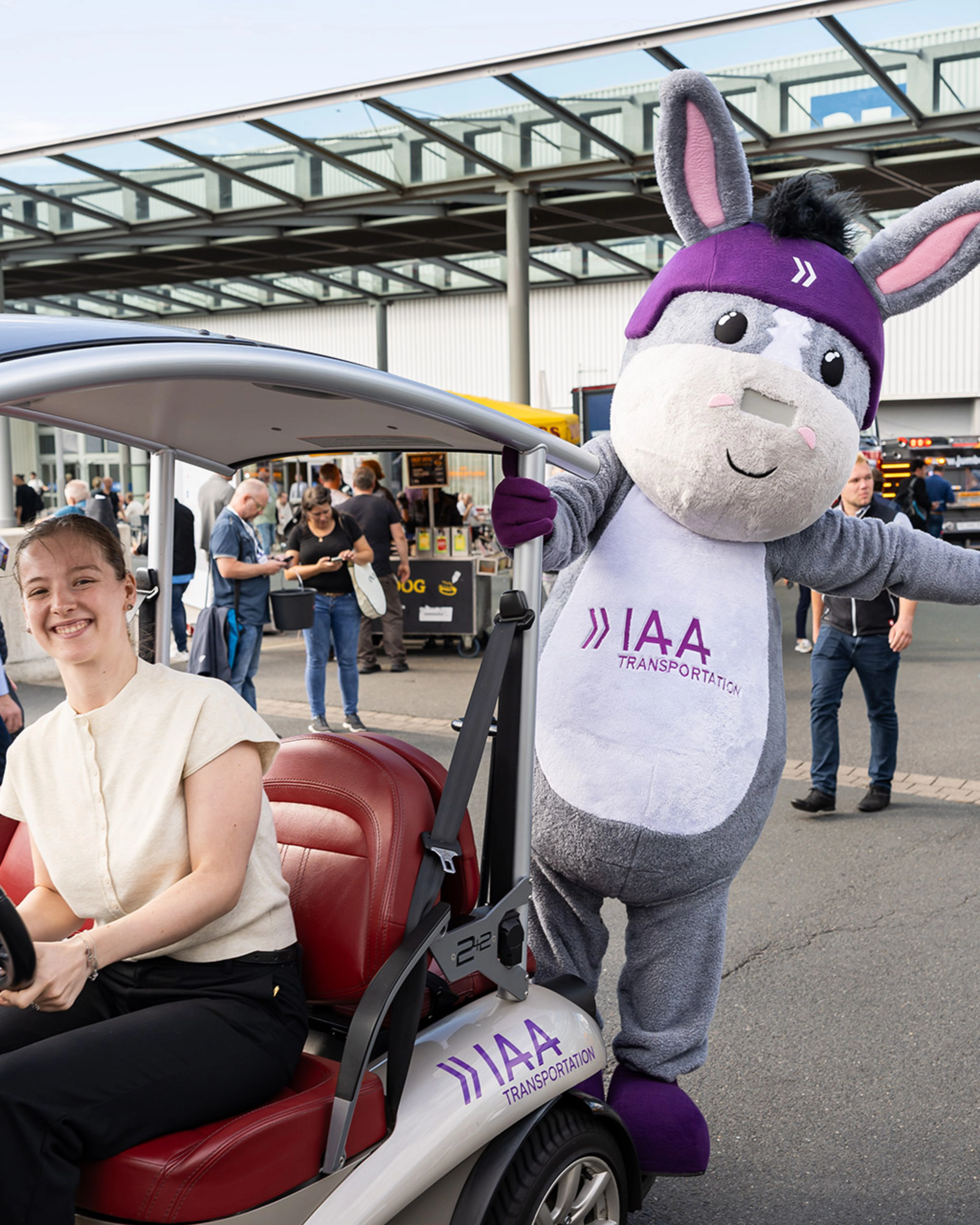 Woman in an IAA vehicle next to the IAA Transportation mascot at the event.