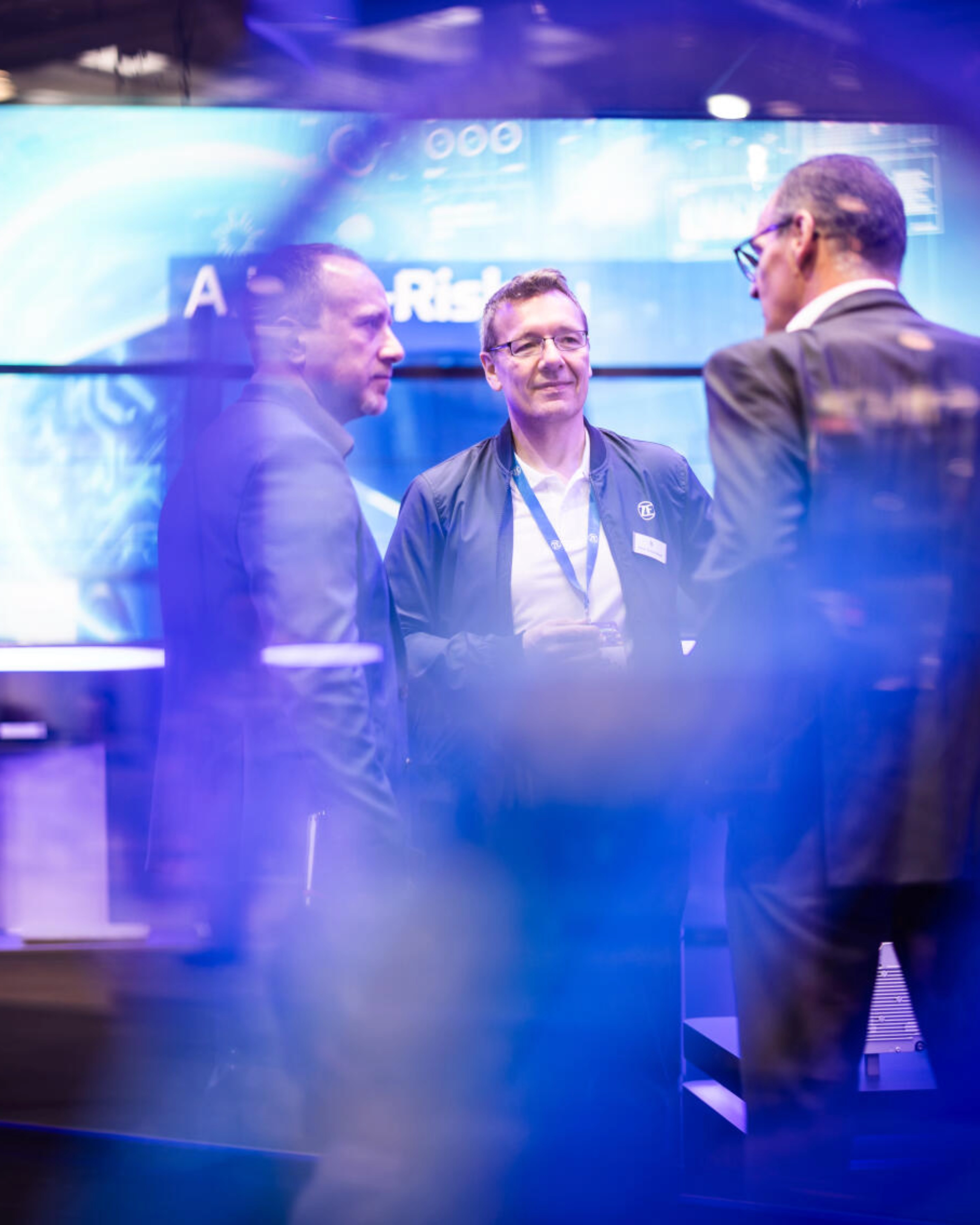 Drei Männer unterhalten sich an einem Messestand für Technologie.