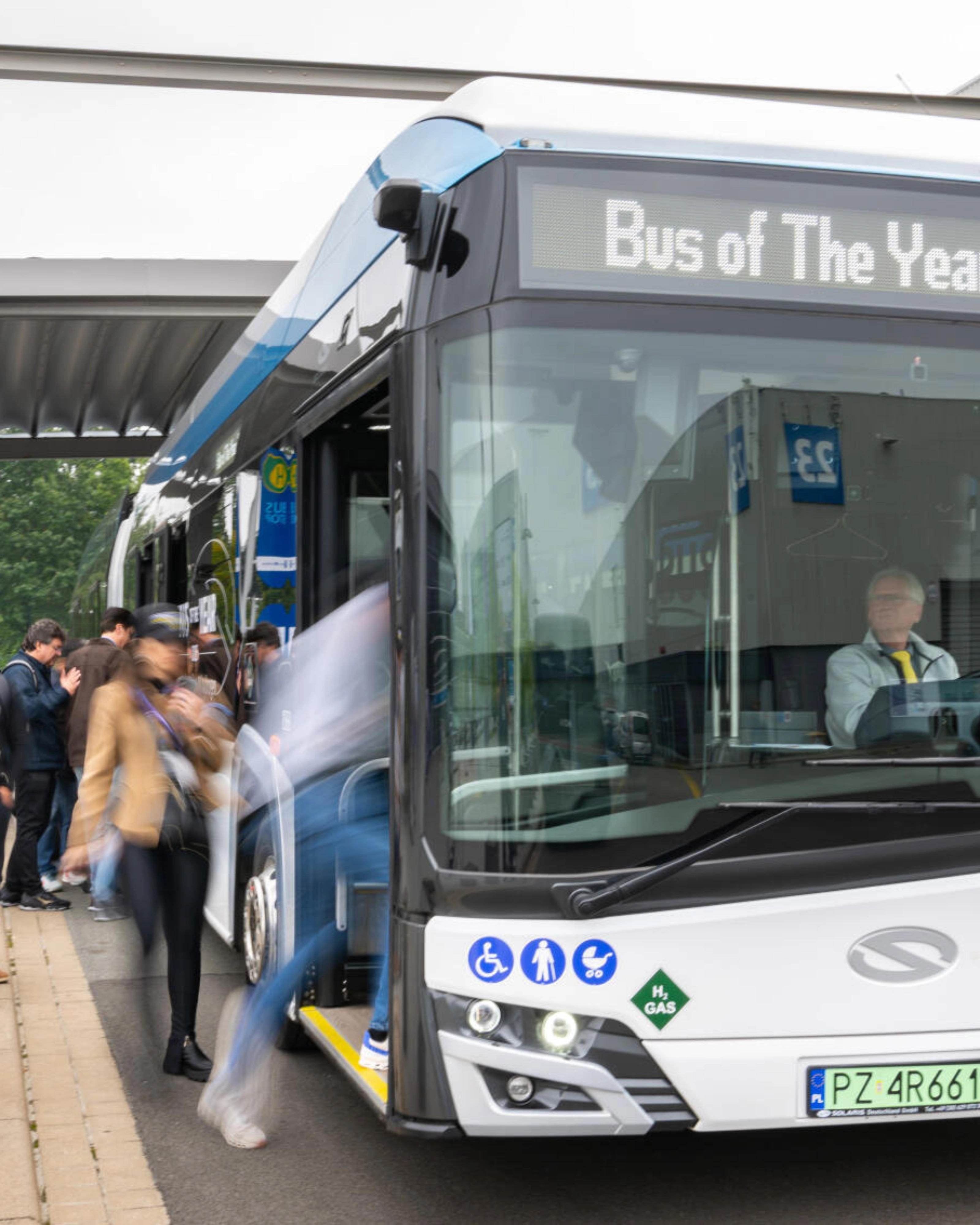 Hydrogen shuttle bus marked “Bus of The Year 2025” at a busy bus stop.