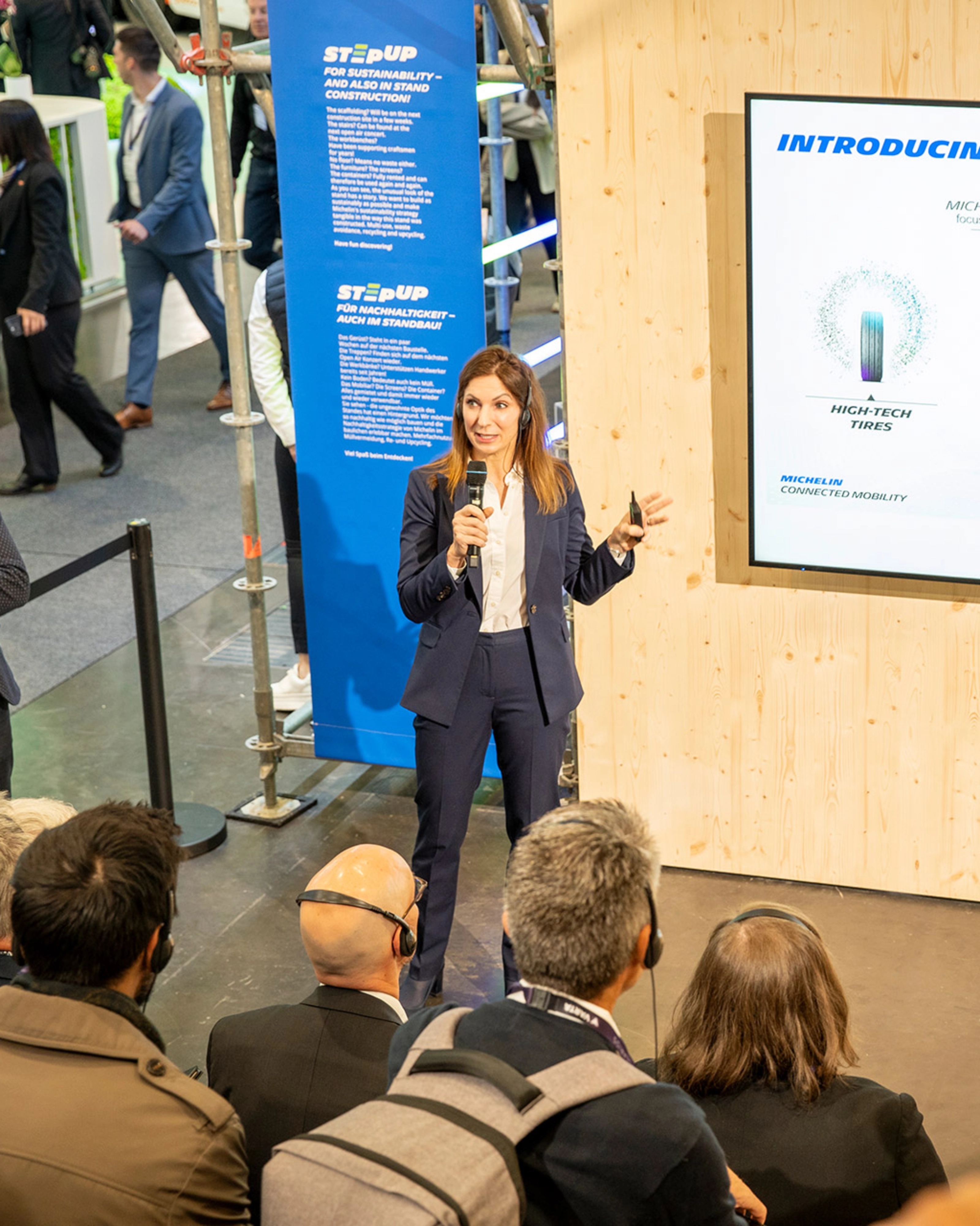 Woman presents Michelin Connected Mobility to audience at trade fair booth.