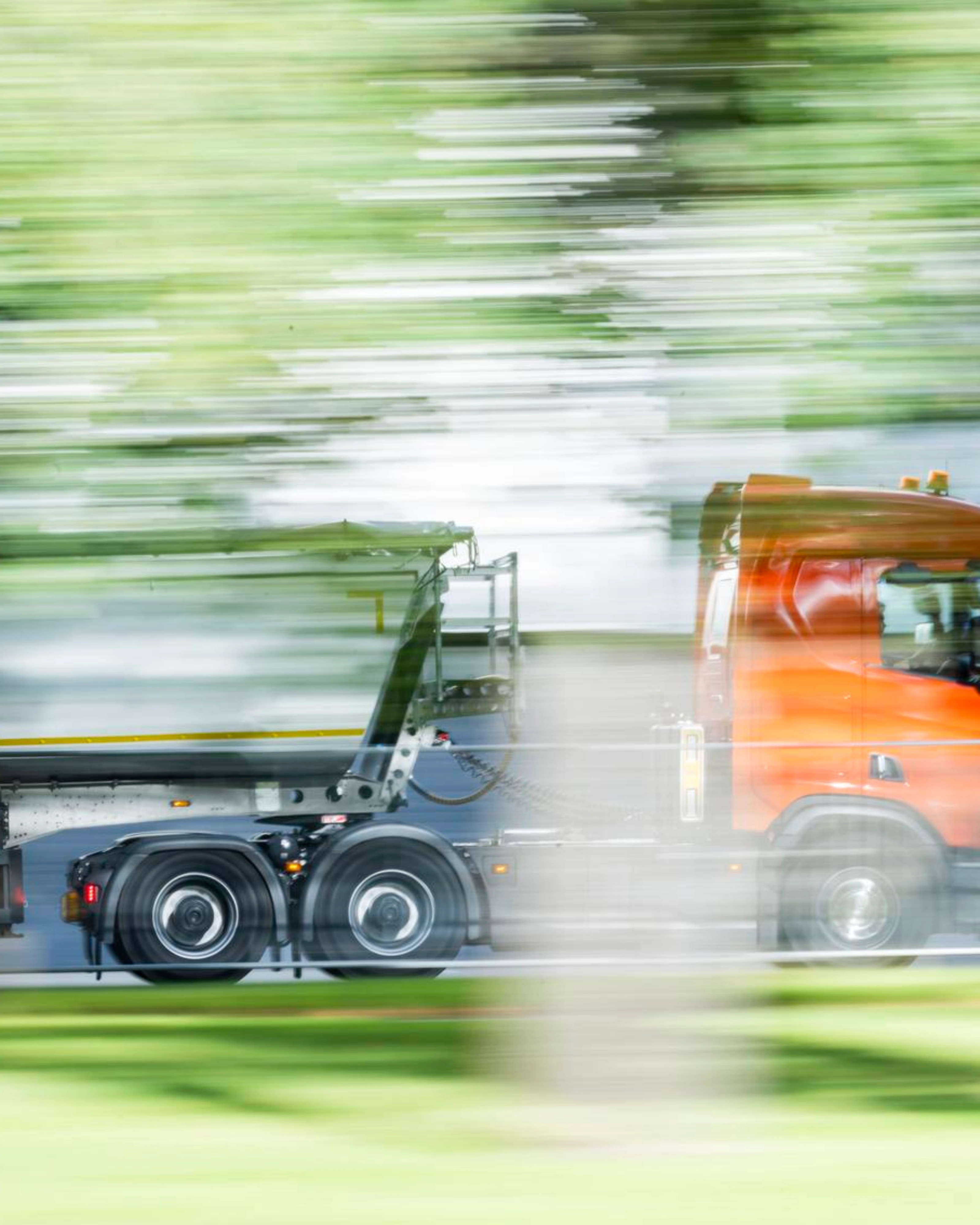 Ein Lkw mit Auflieger fährt auf einer von Grün umgebenen Straße.