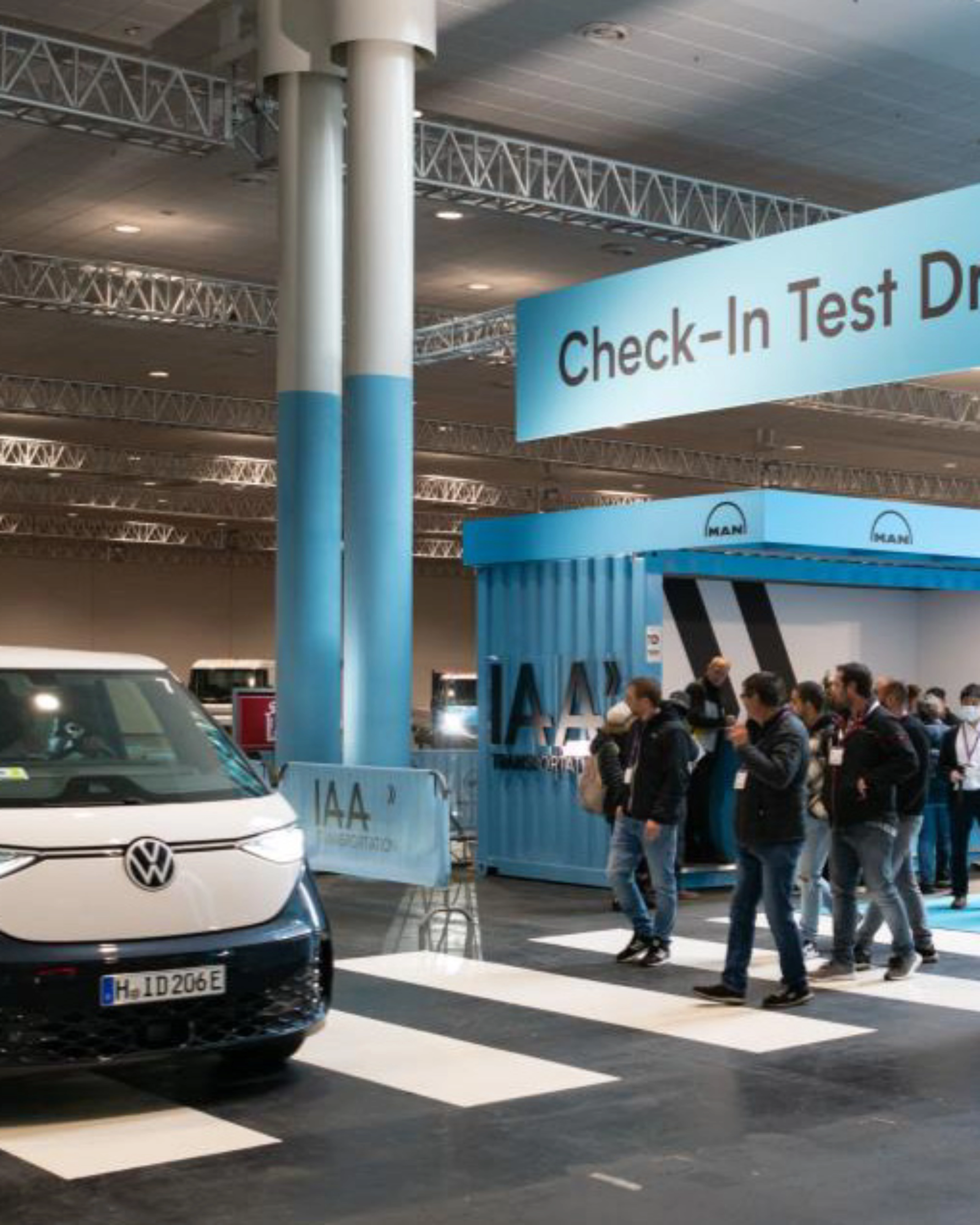 Exhibition hall scene with a Volkswagen van driving past the IAA Transportation check-in for test drives.