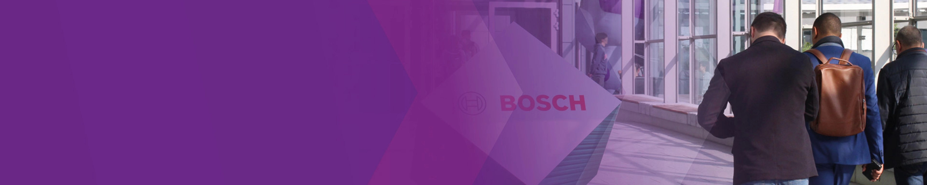 Three men walk through a modern glass corridor with a Bosch logo sign.