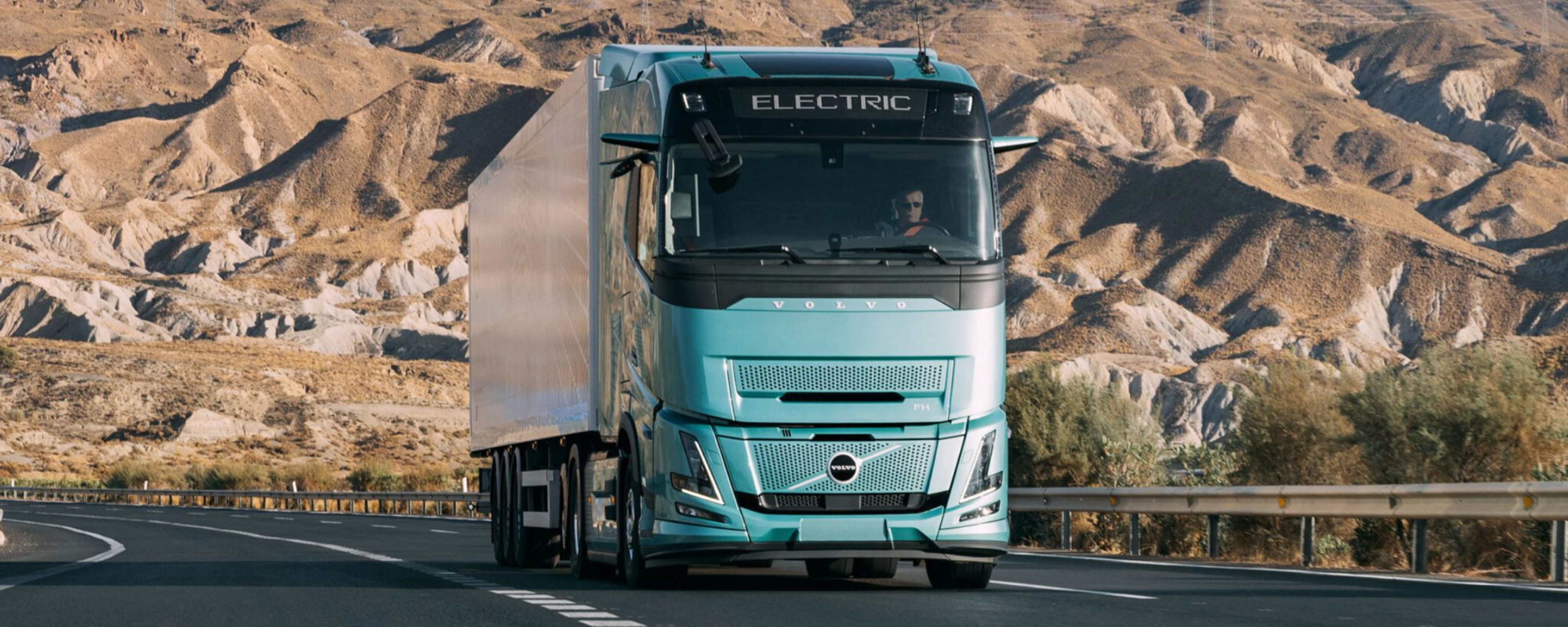 Volvo truck driving on a highway through a rocky desert landscape.