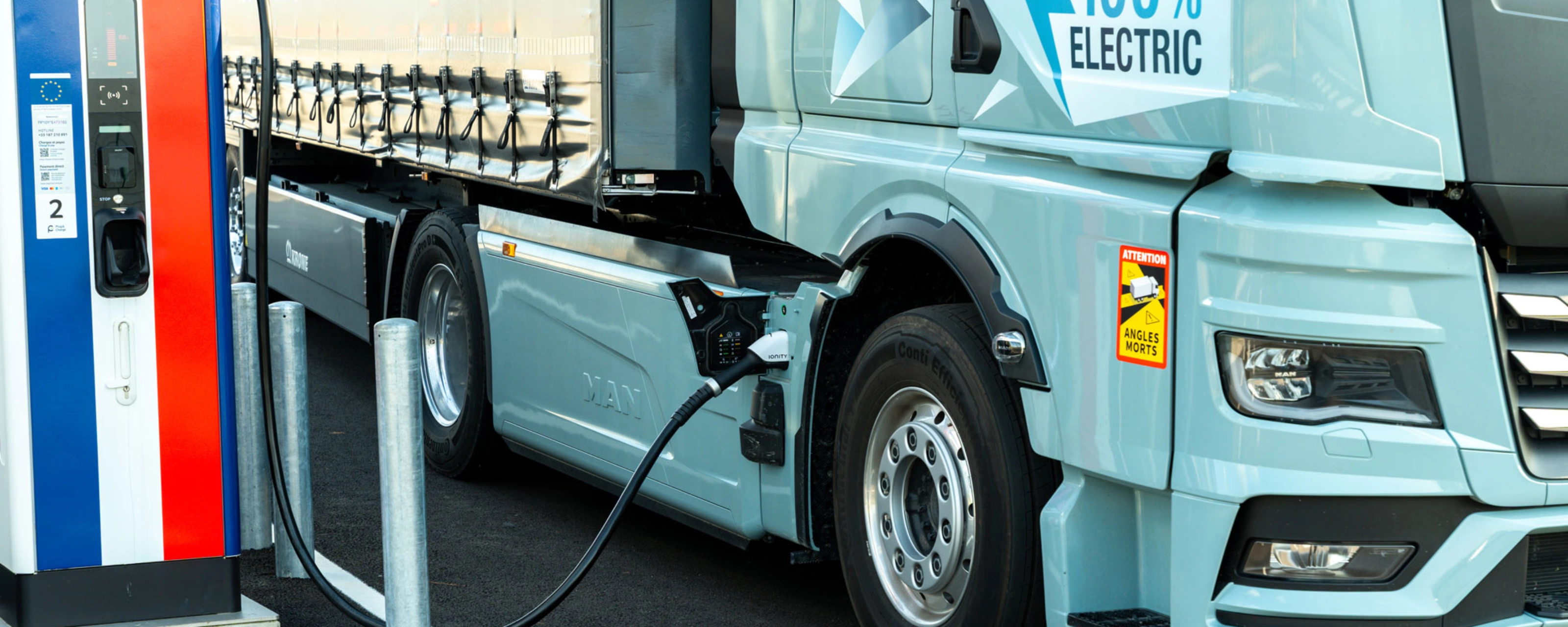 Electric truck charging at a public station, labeled 100% electric.