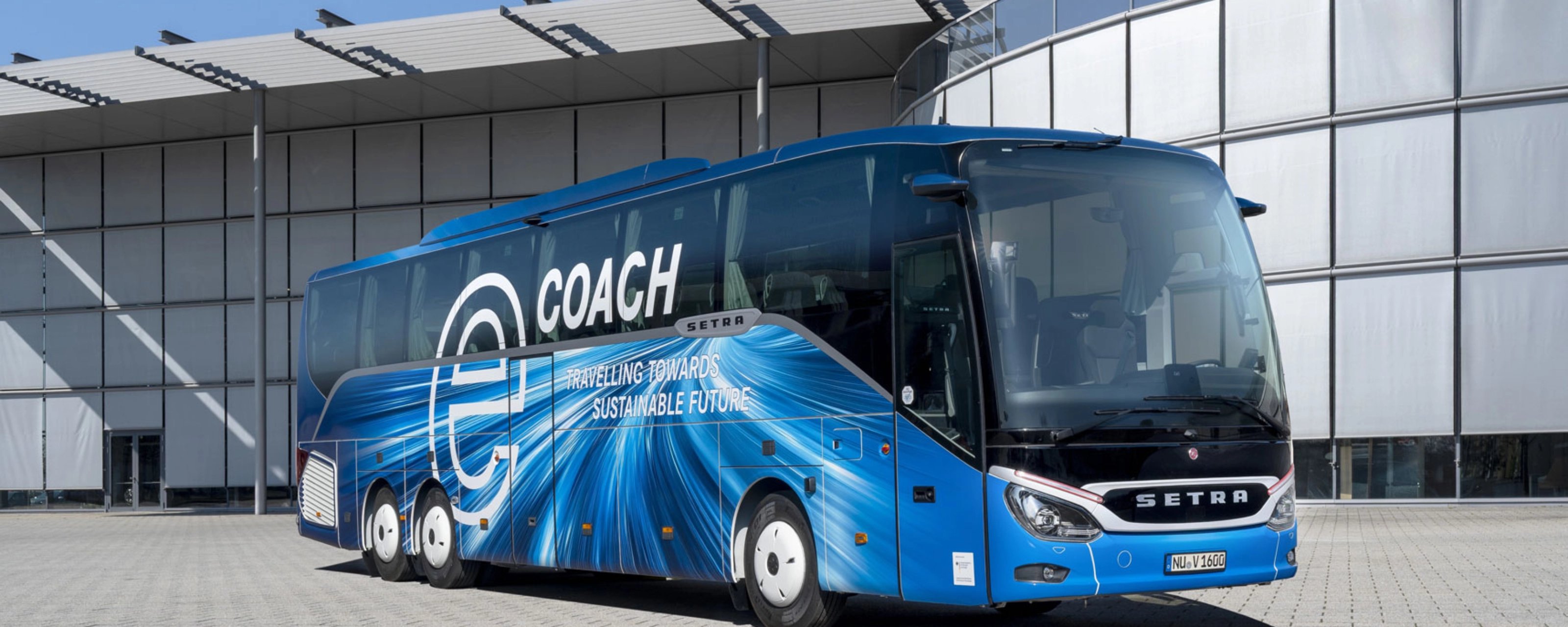 Blauer Setra-Reisebus mit Nachhaltigkeits-Slogan vor modernem Gebäude.