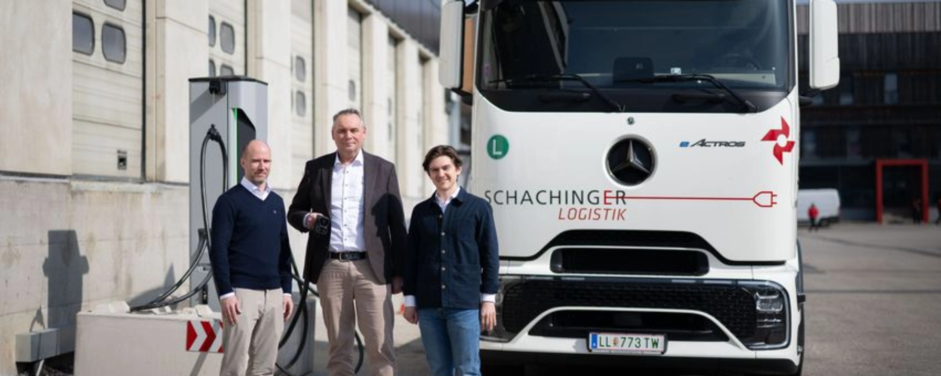 Three men standing in front of a white truck outside an industrial building.