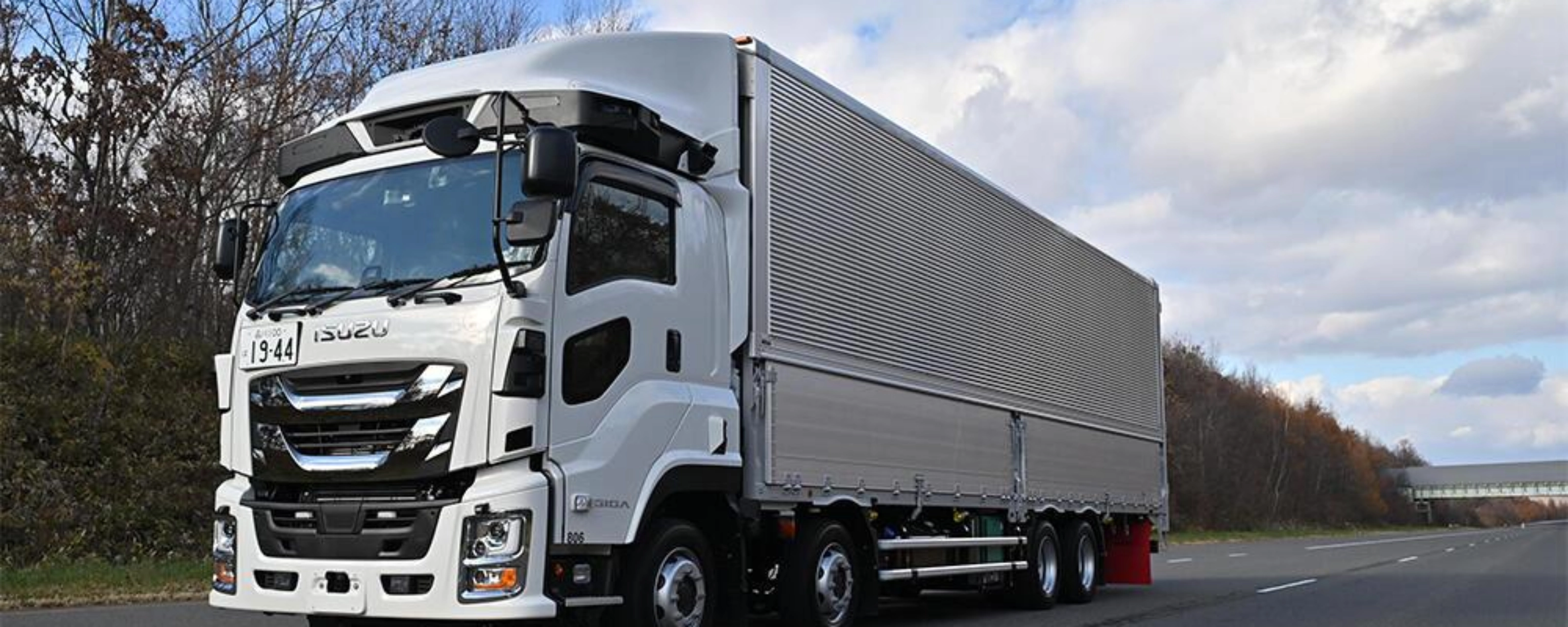 White semi-truck with trailer driving on a highway under a cloudy sky.
