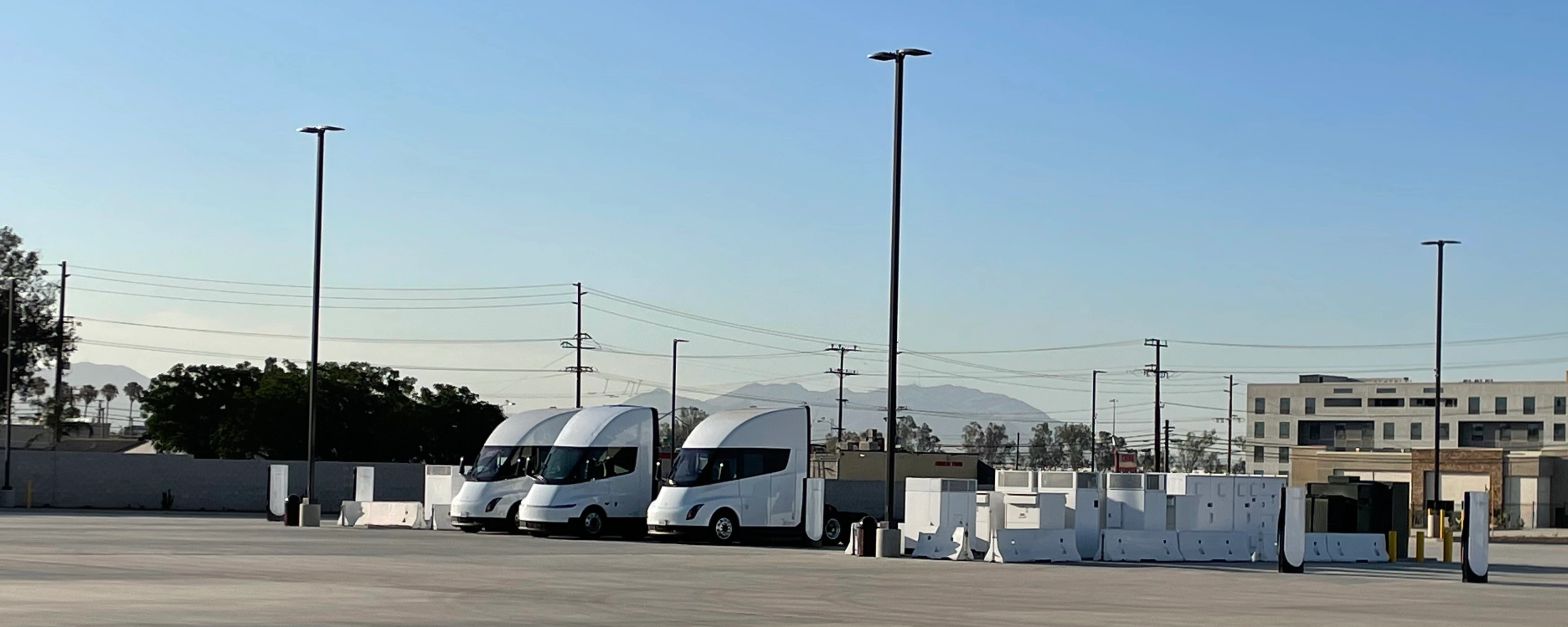 Three white electric trucks are parked at a charging station.