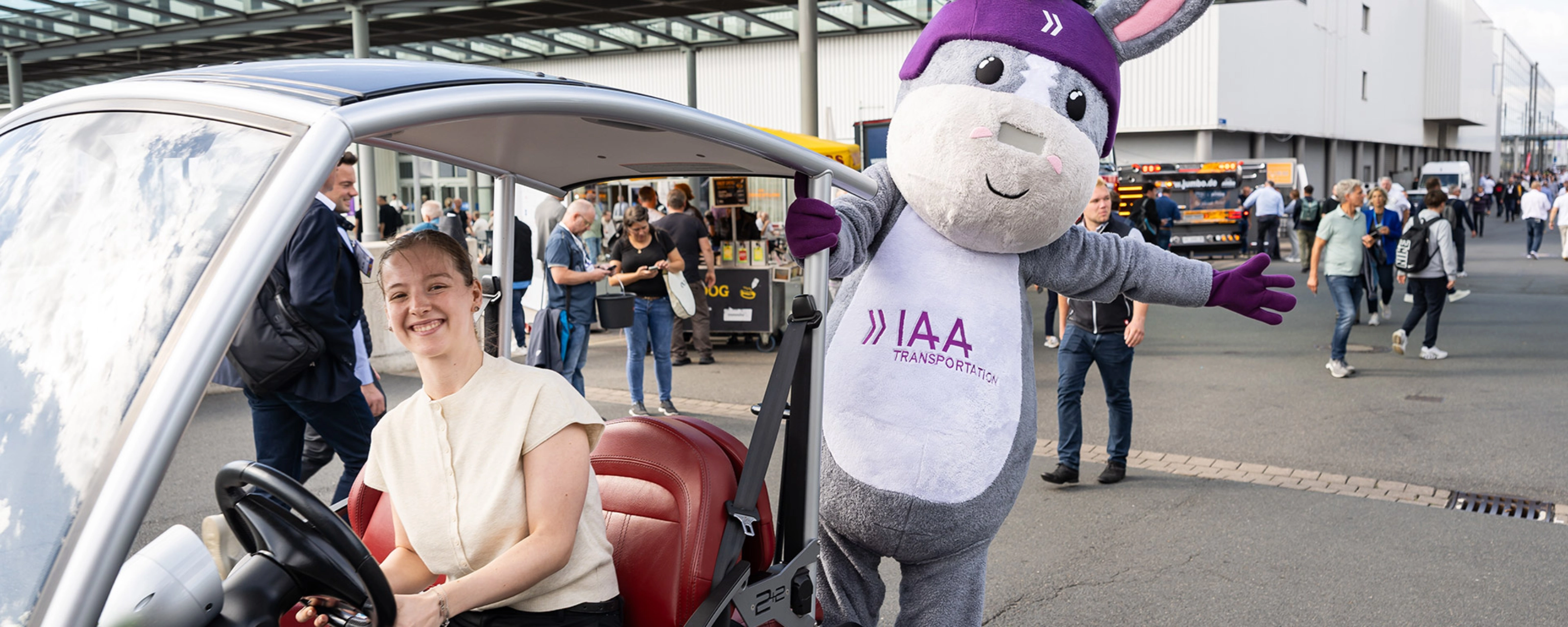 Frau in einem IAA-Fahrzeug neben dem IAA Transportation Maskottchen auf der Messe.