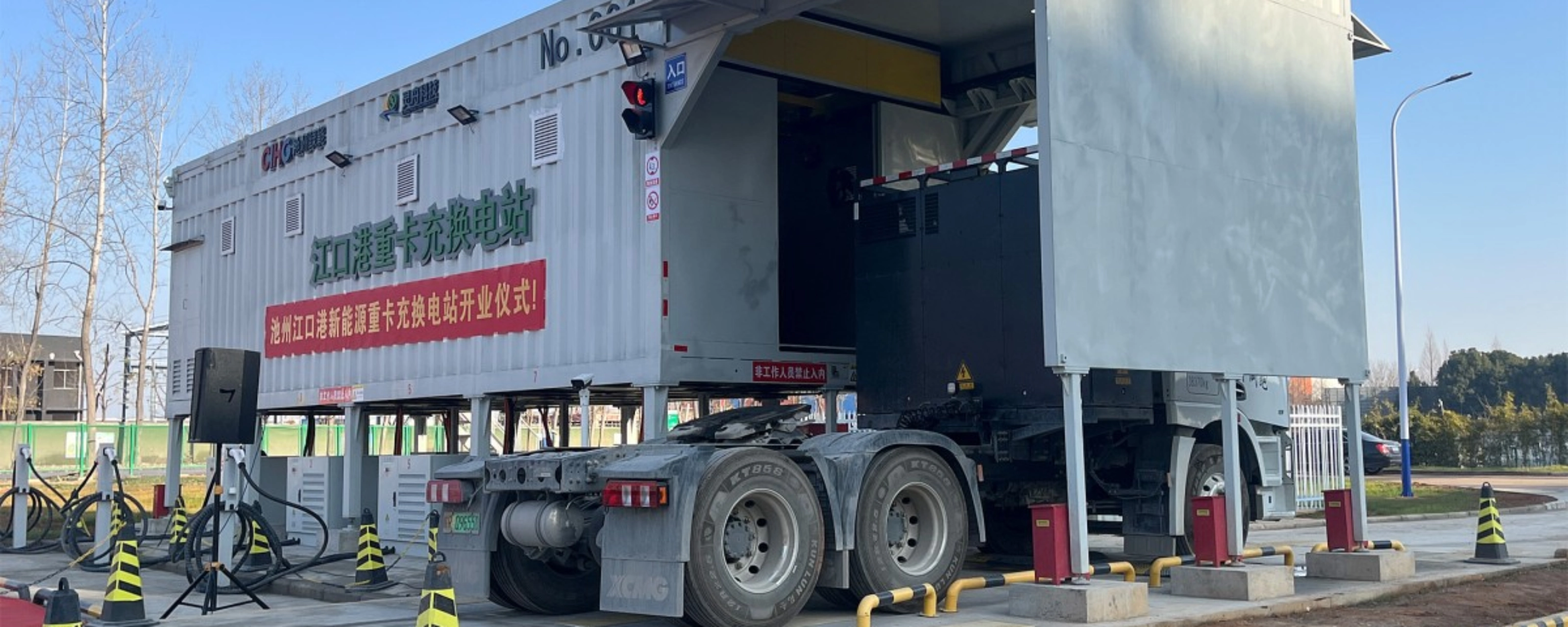 Truck at battery swap station with container module in industrial area.