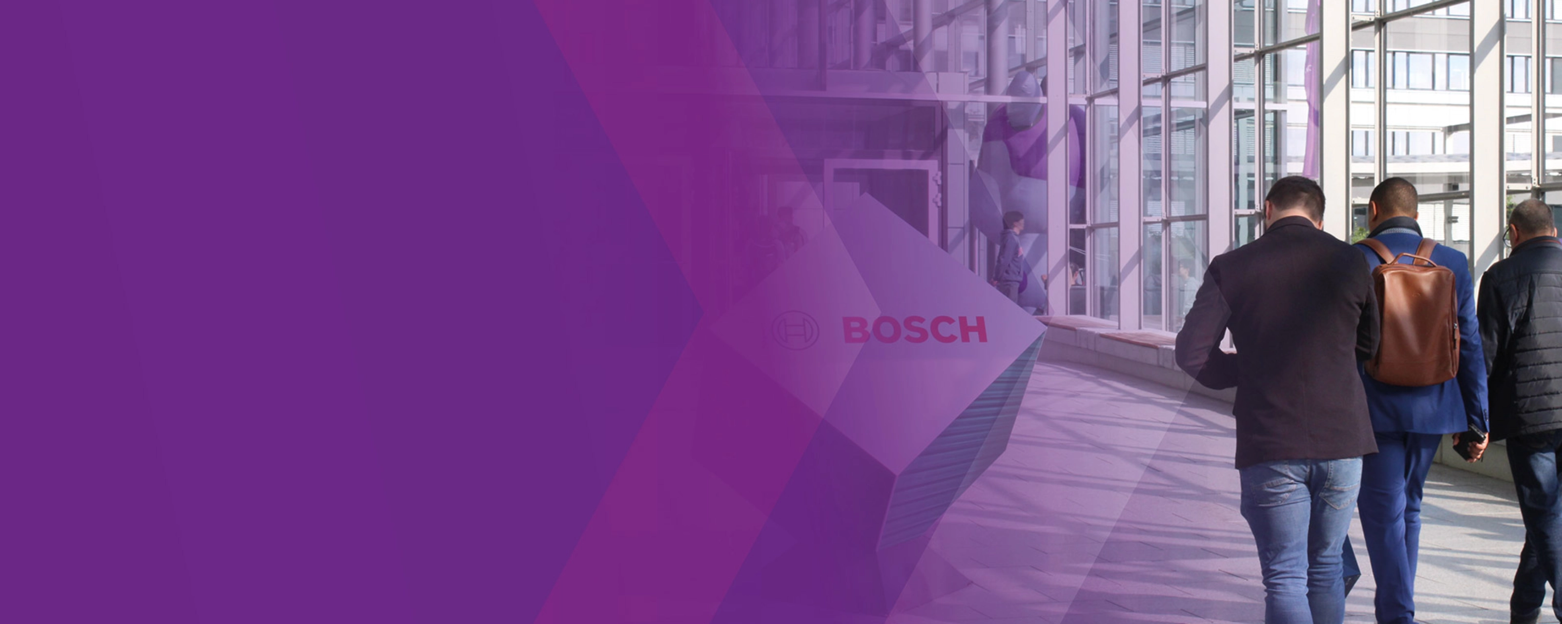 Three men walk through a modern glass corridor with a Bosch logo sign.