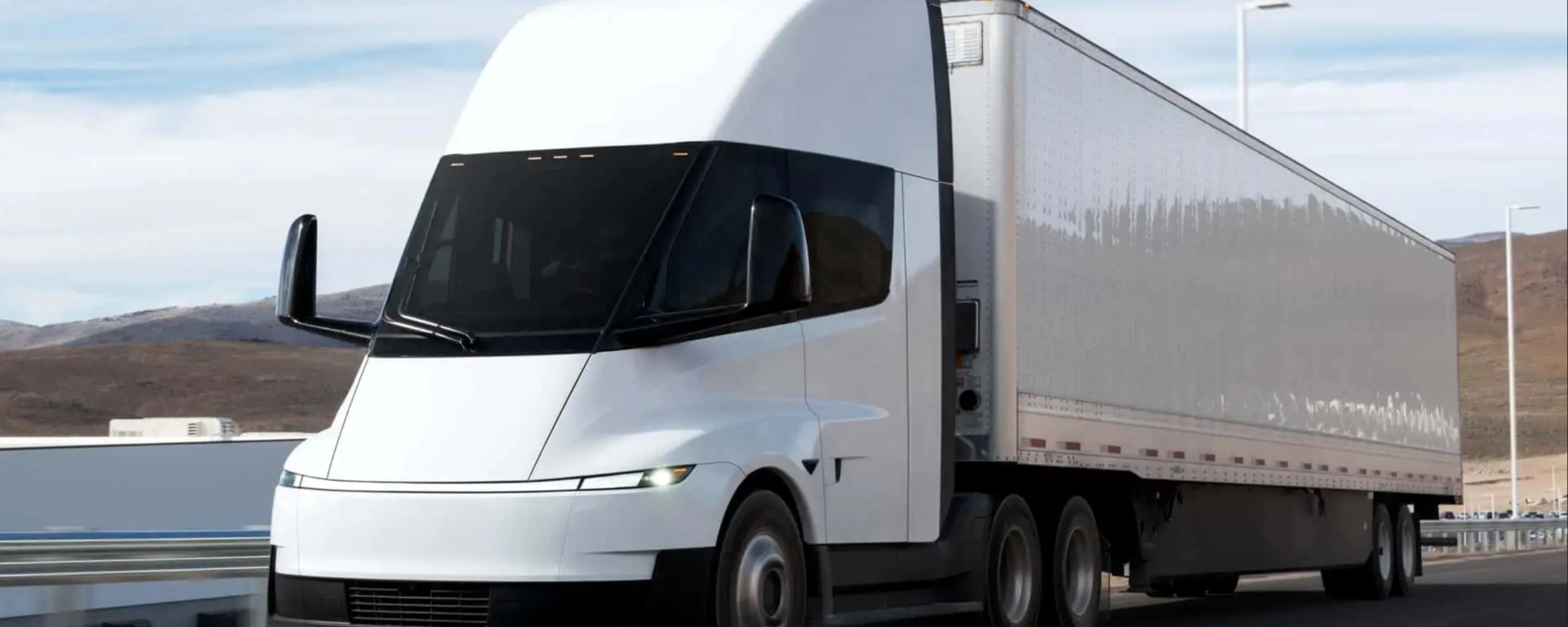 Electric semi-truck driving on a highway in a rural landscape.