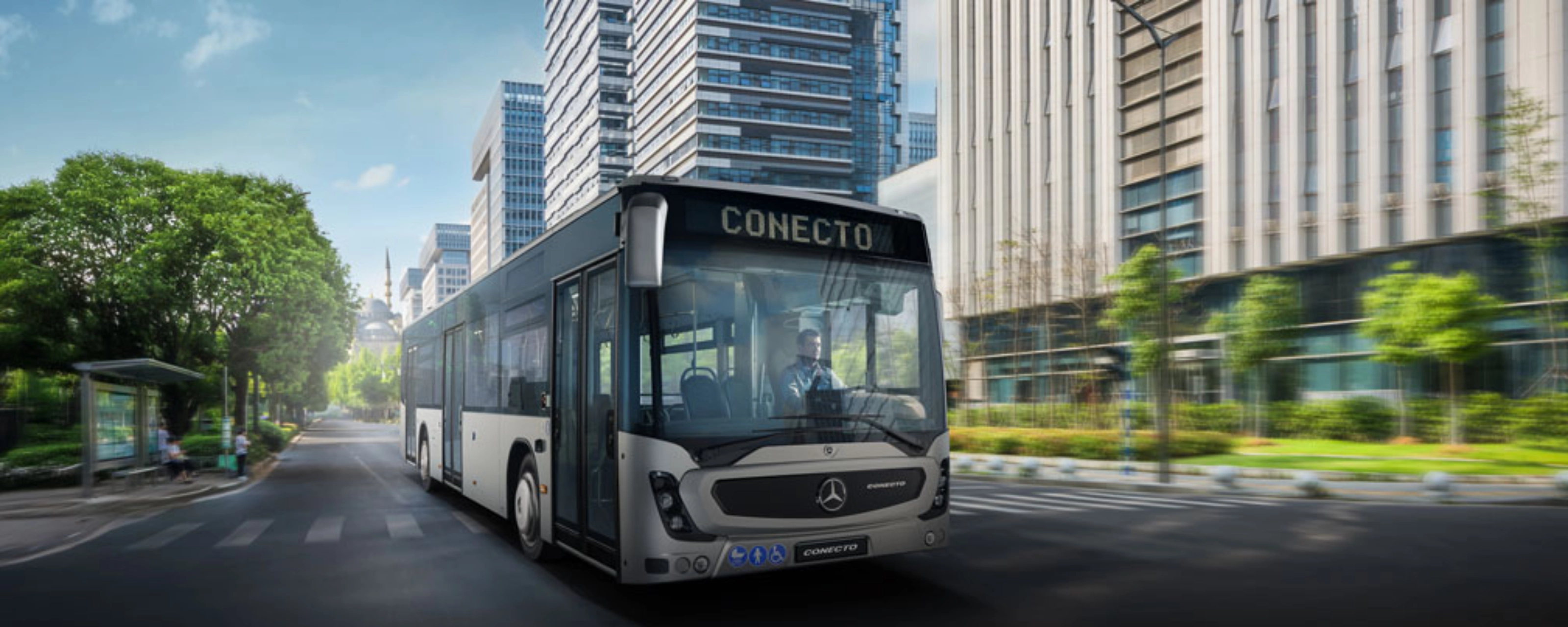 Modern city bus driving on a wide street between tall office buildings.