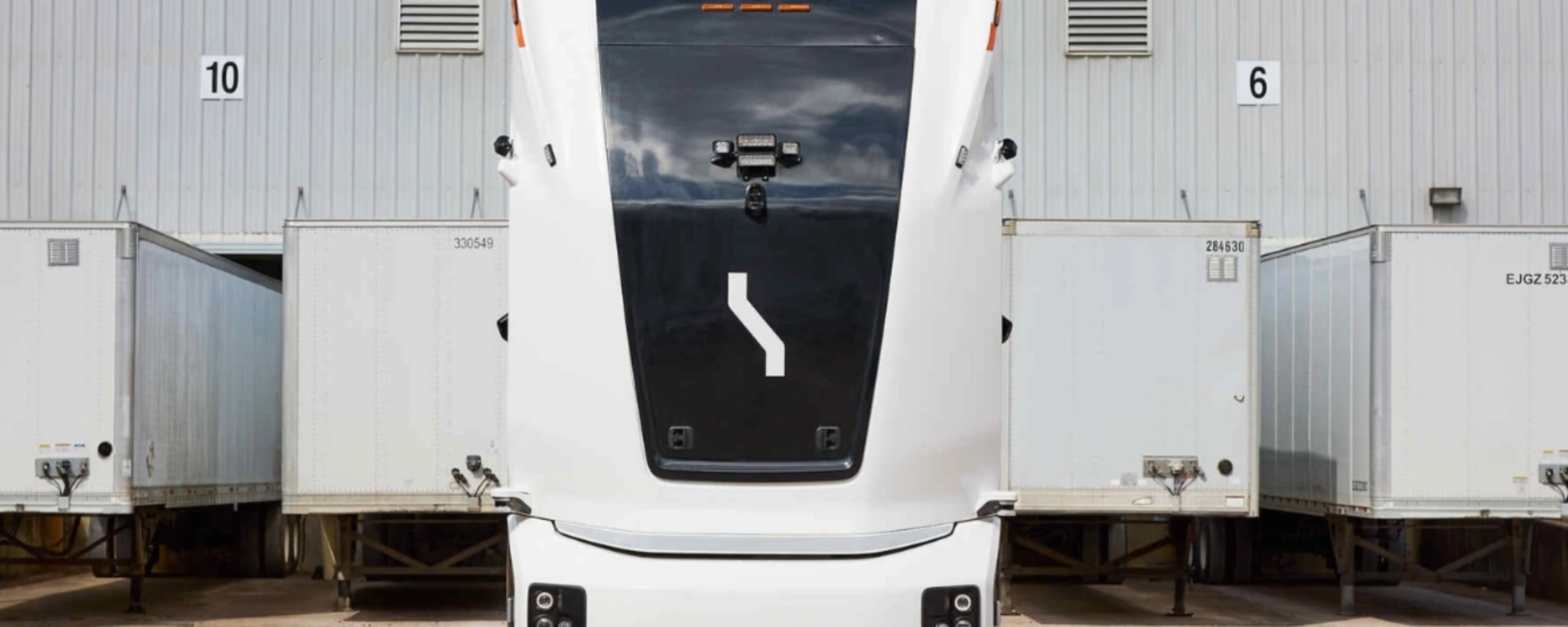 Einride autonomous electric truck in front of a warehouse with trailers.