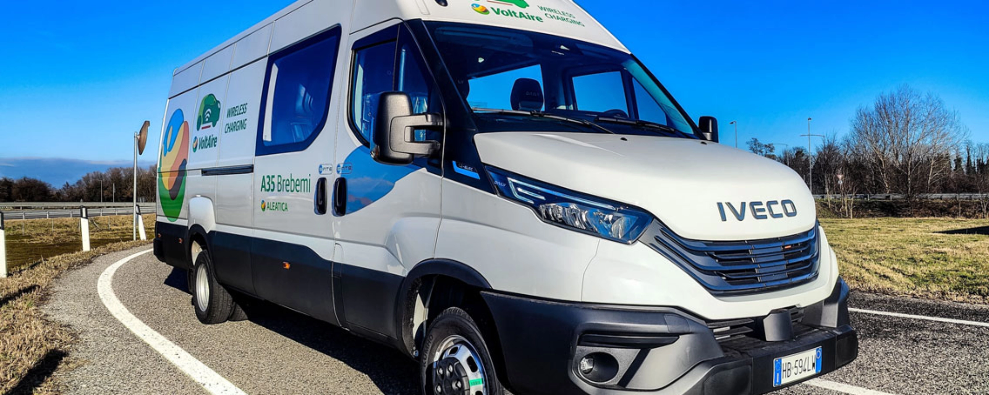 Ein weißer Iveco-Transporter fährt auf einer kurvigen Straße bei blauem Himmel.