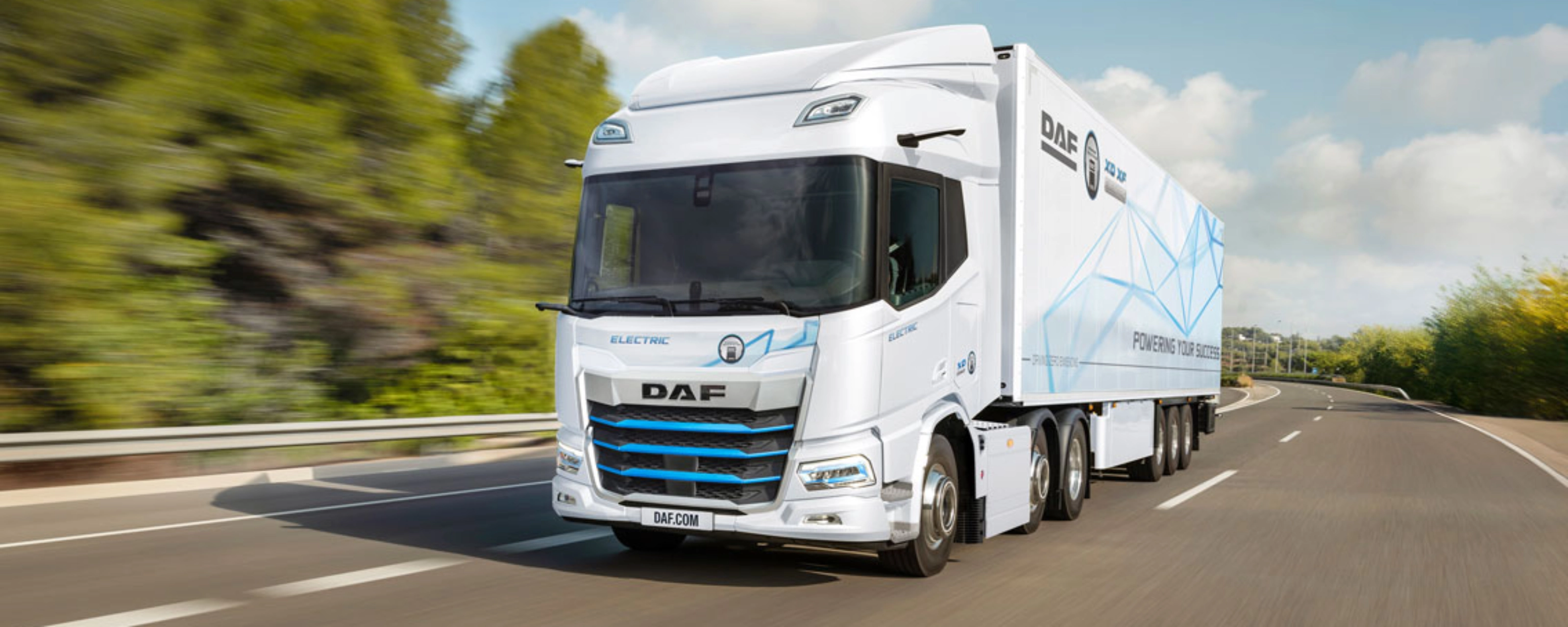 A white DAF electric truck is driving on a curved highway surrounded by greenery.