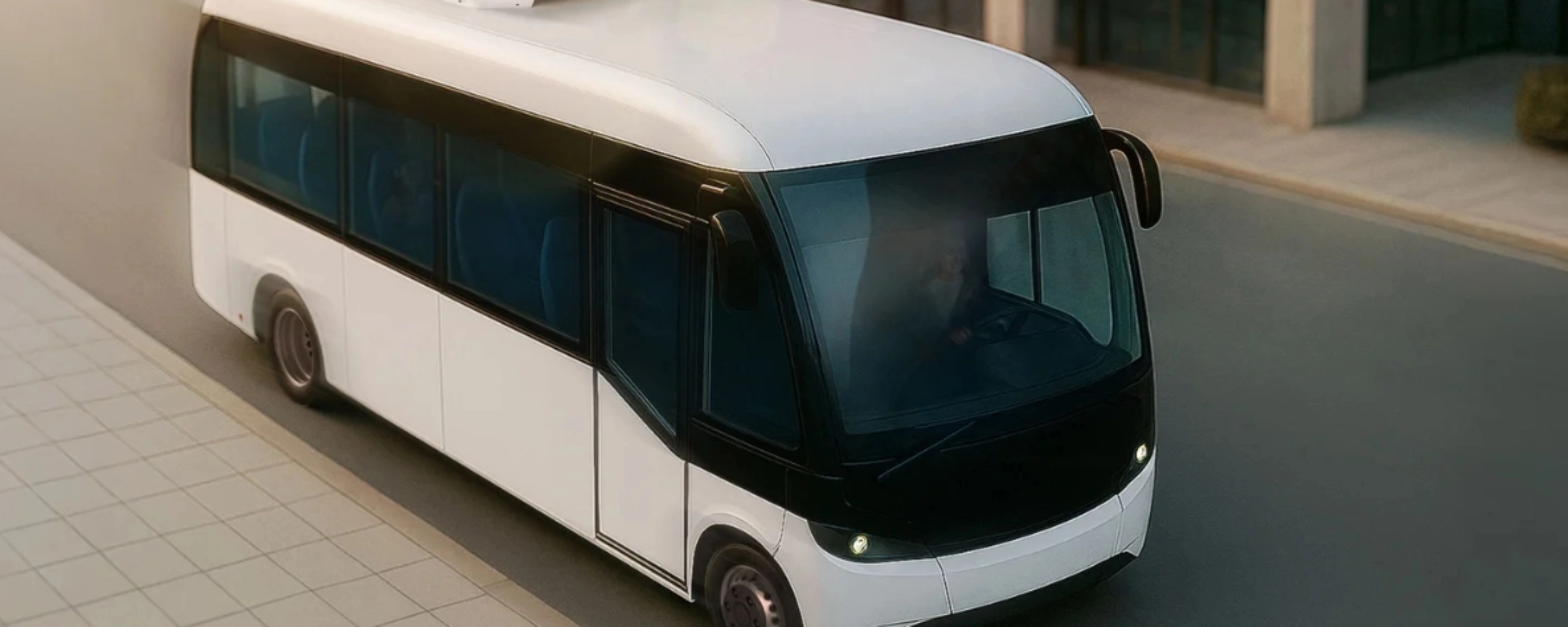 Small white autonomous shuttle bus driving on a city street, viewed from above.
