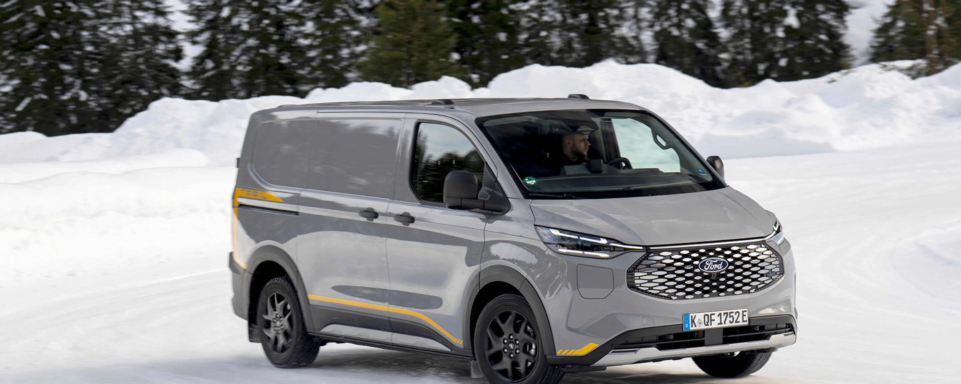 Grey Ford electric van driving on a snowy road with forest in the background.