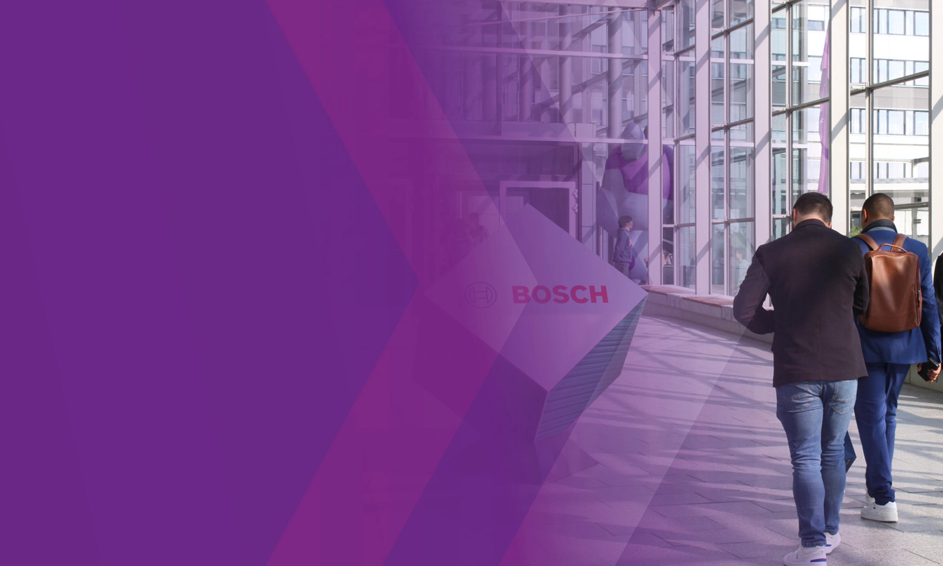 Three men walk through a modern glass corridor with a Bosch logo sign.