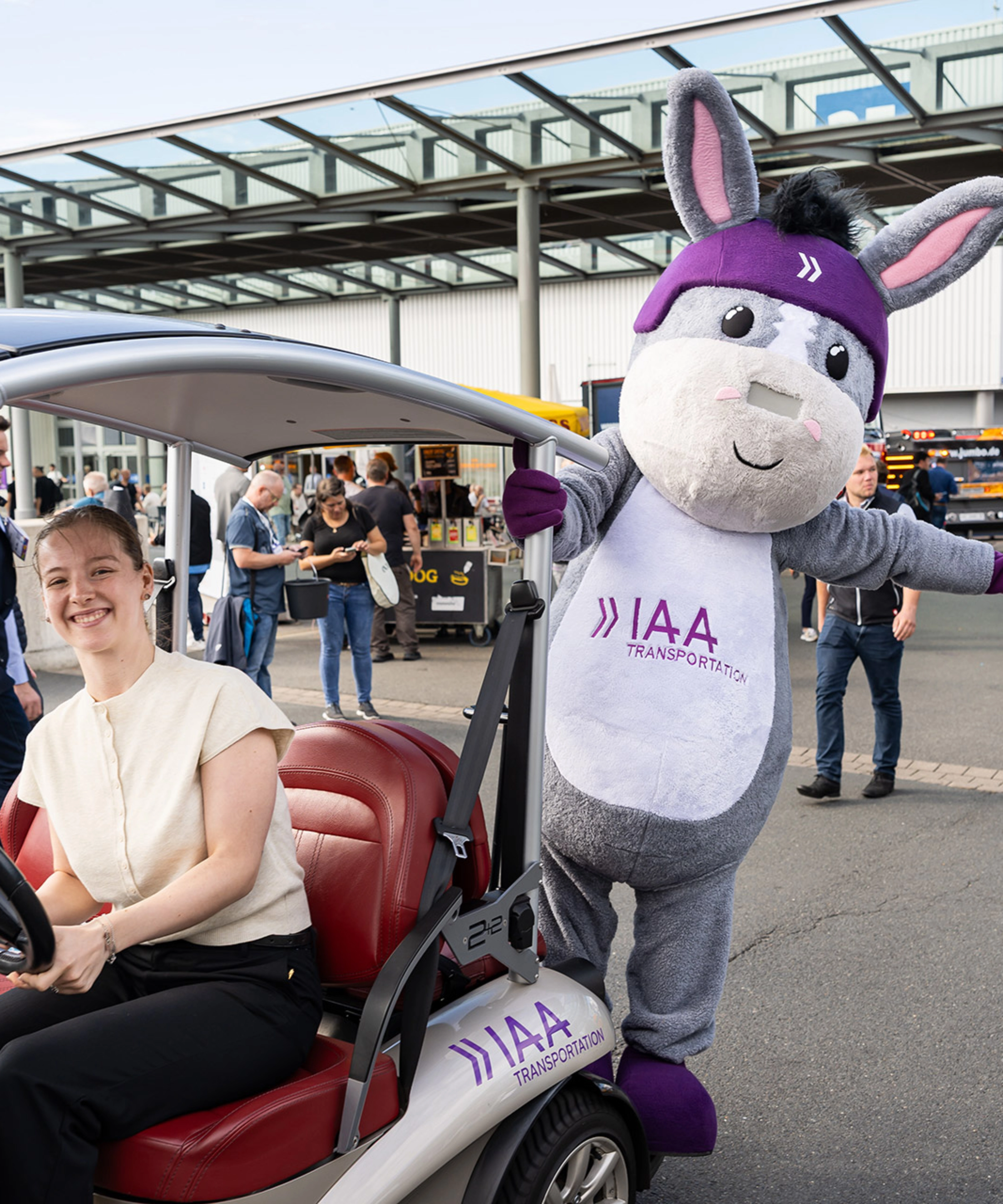 Woman in an IAA vehicle next to the IAA Transportation mascot at the event.