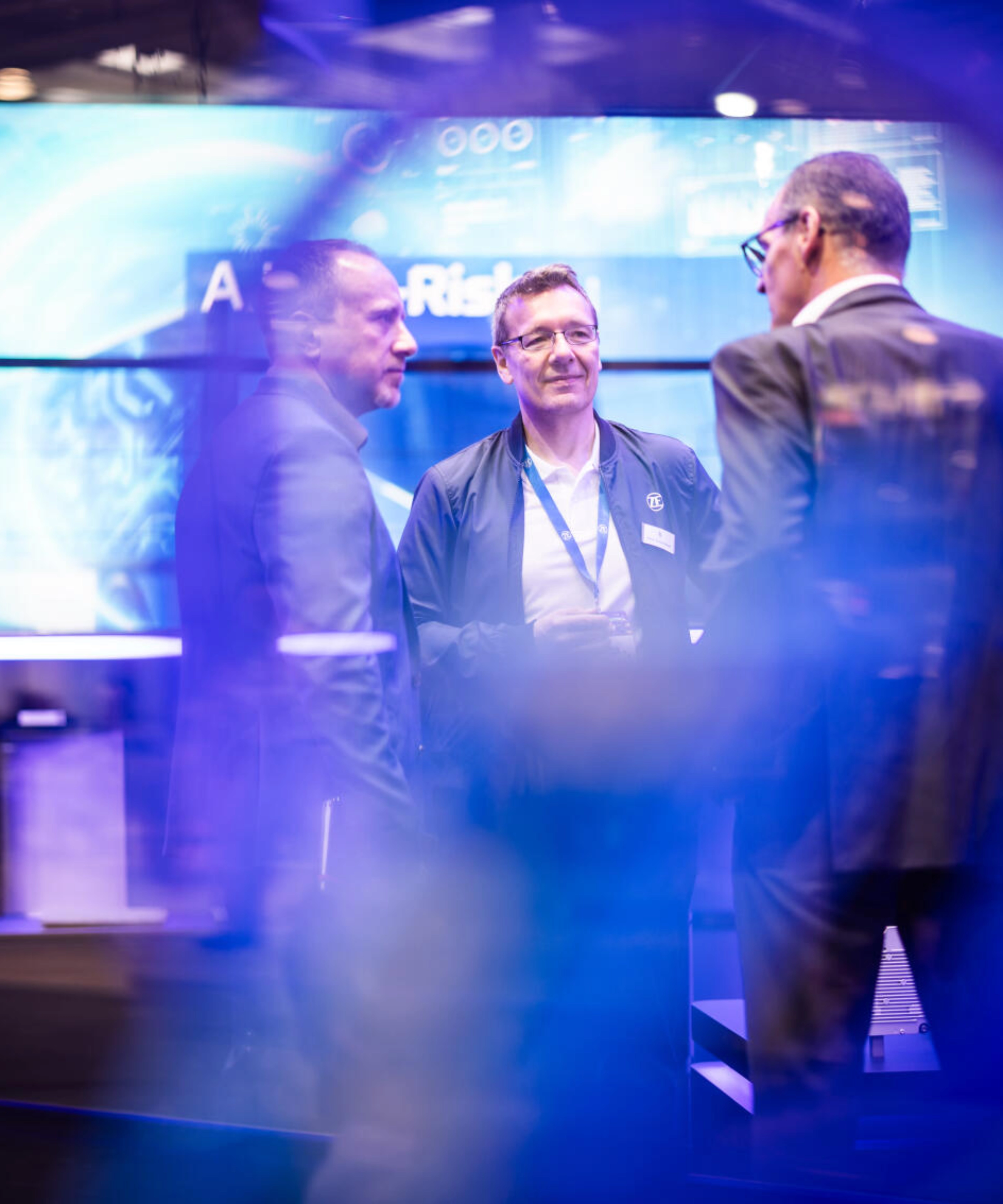 Drei Männer unterhalten sich an einem Messestand für Technologie.