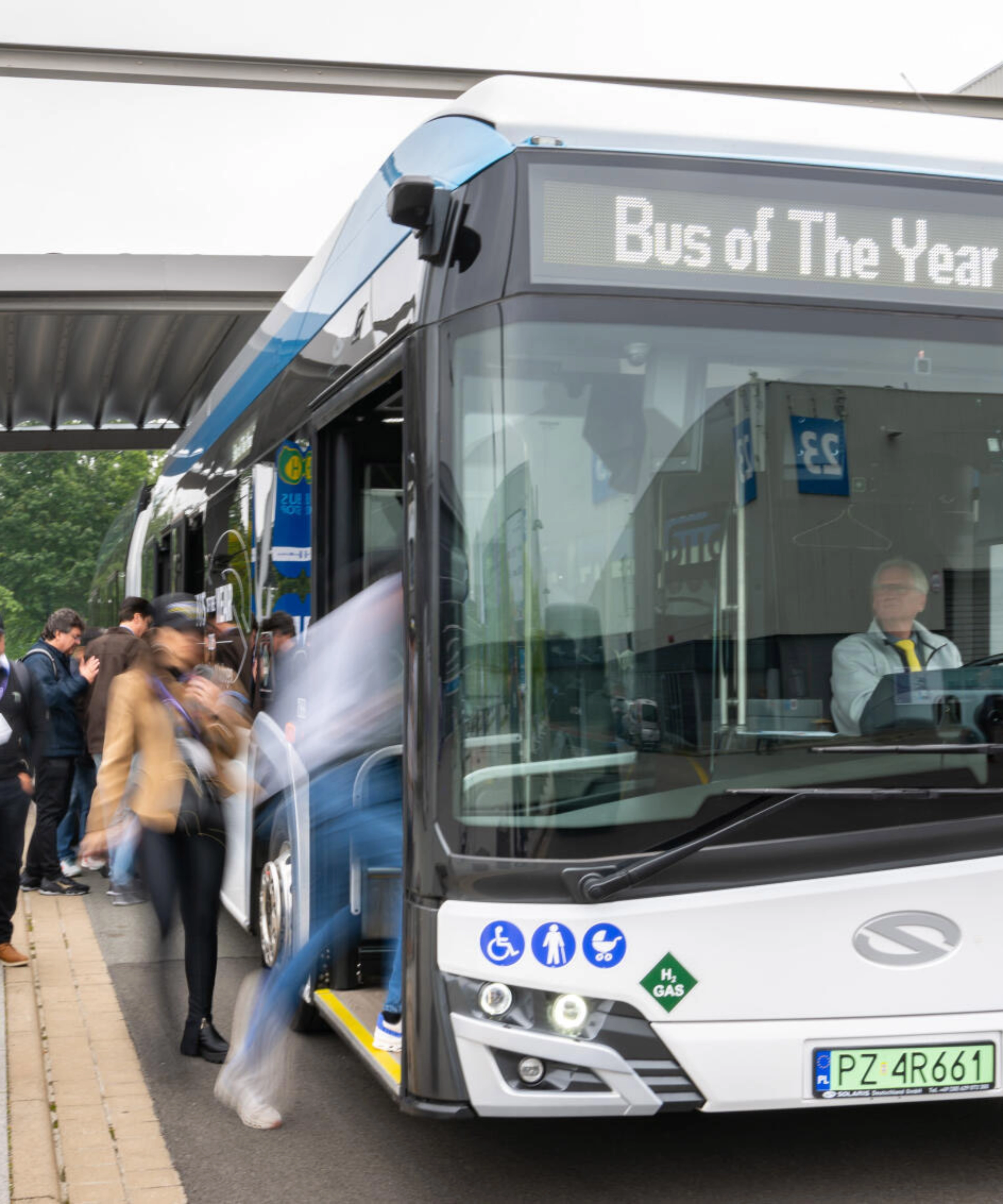 Hydrogen shuttle bus marked “Bus of The Year 2025” at a busy bus stop.