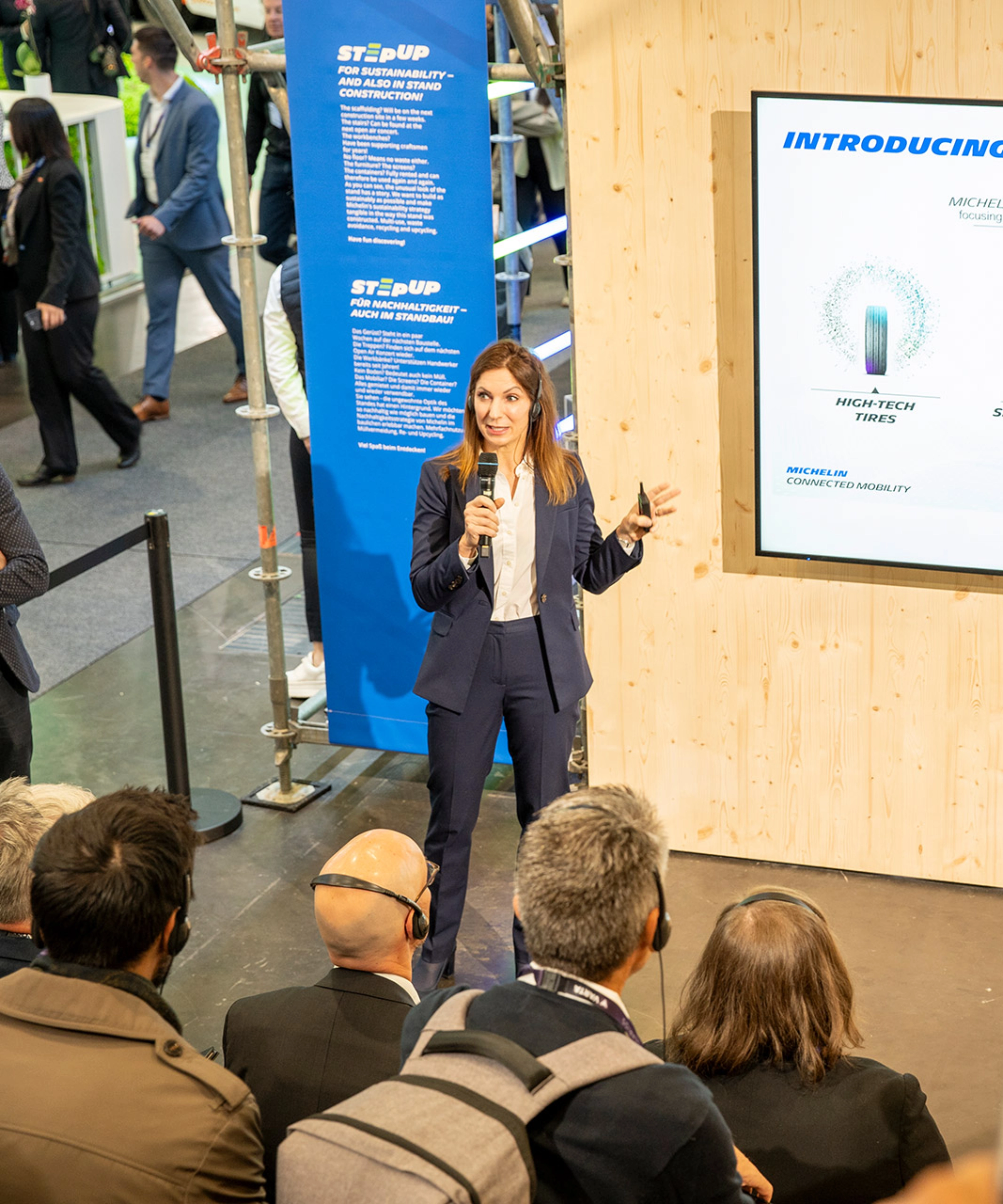 Woman presents Michelin Connected Mobility to audience at trade fair booth.