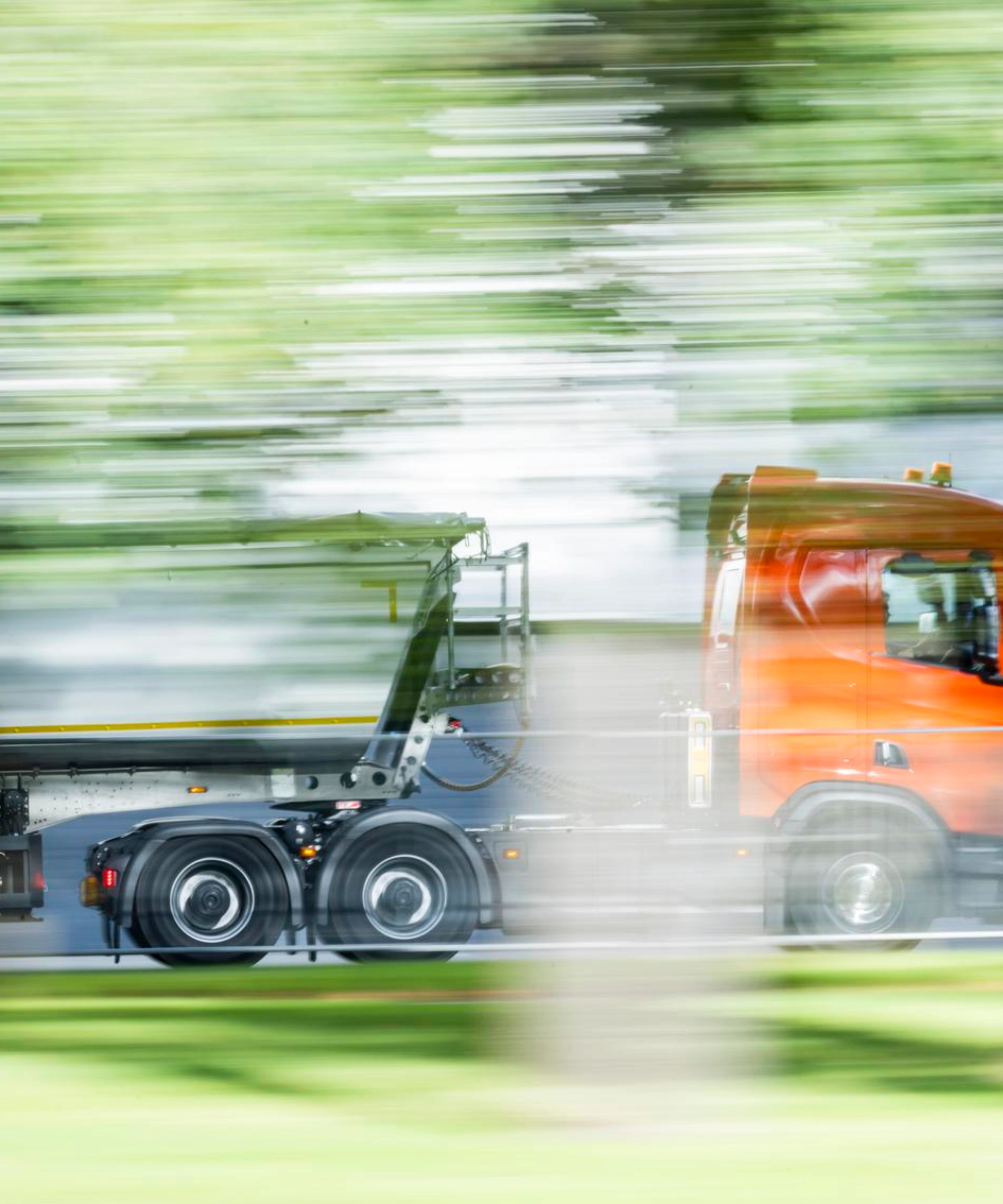 Ein Lkw mit Auflieger fährt auf einer von Grün umgebenen Straße.