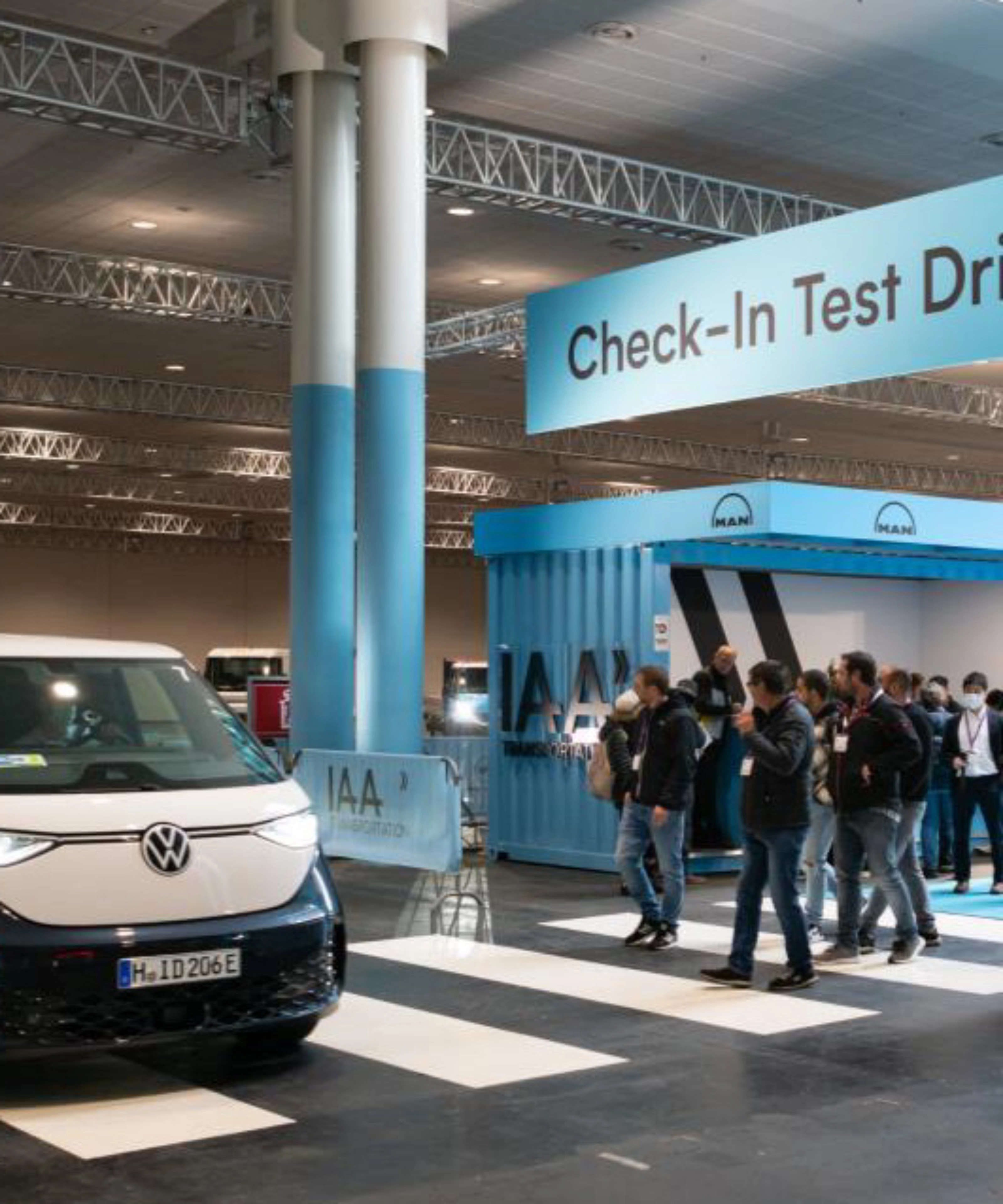 Exhibition hall scene with a Volkswagen van driving past the IAA Transportation check-in for test drives.