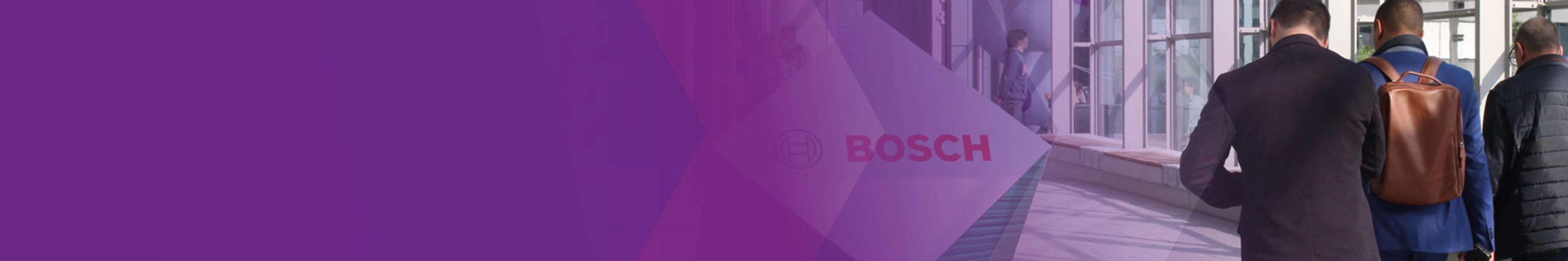 Three men walk through a modern glass corridor with a Bosch logo sign.