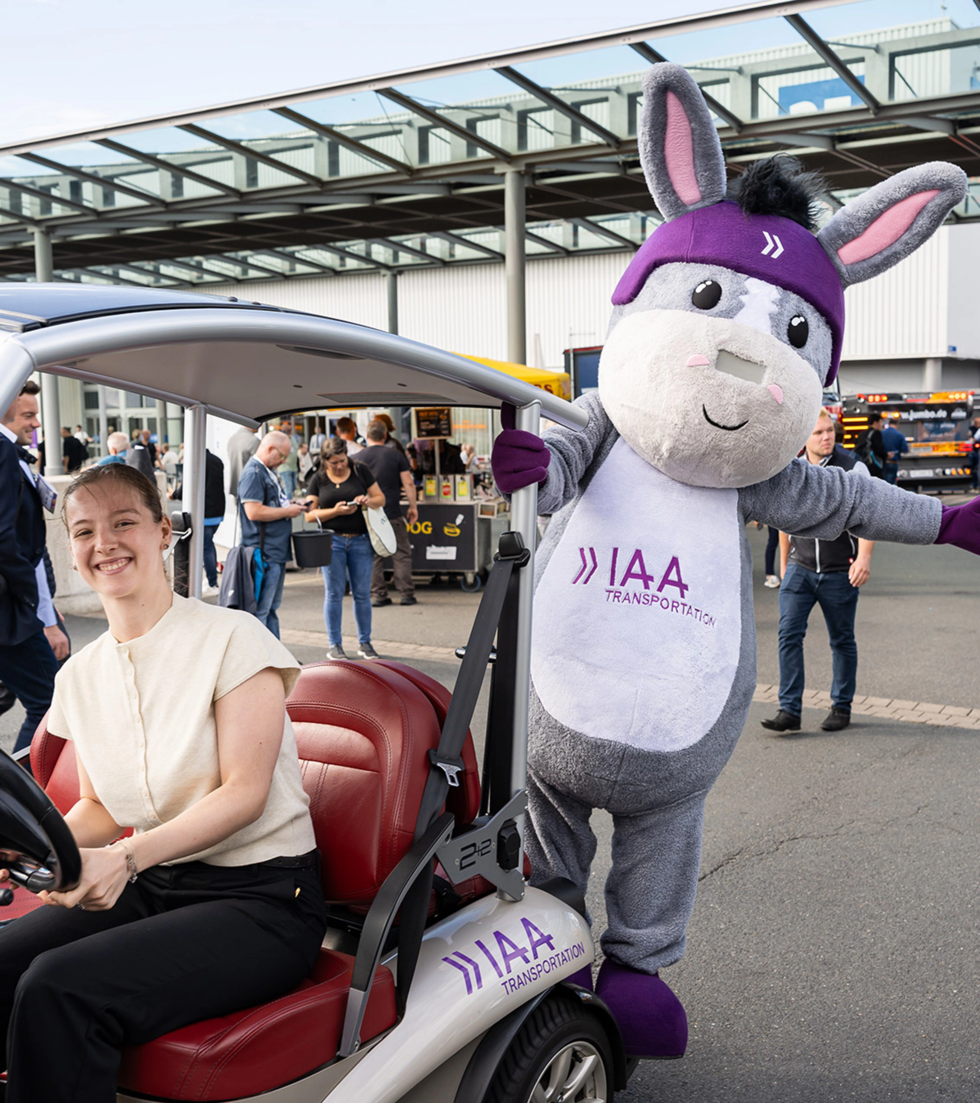 Woman in an IAA vehicle next to the IAA Transportation mascot at the event.