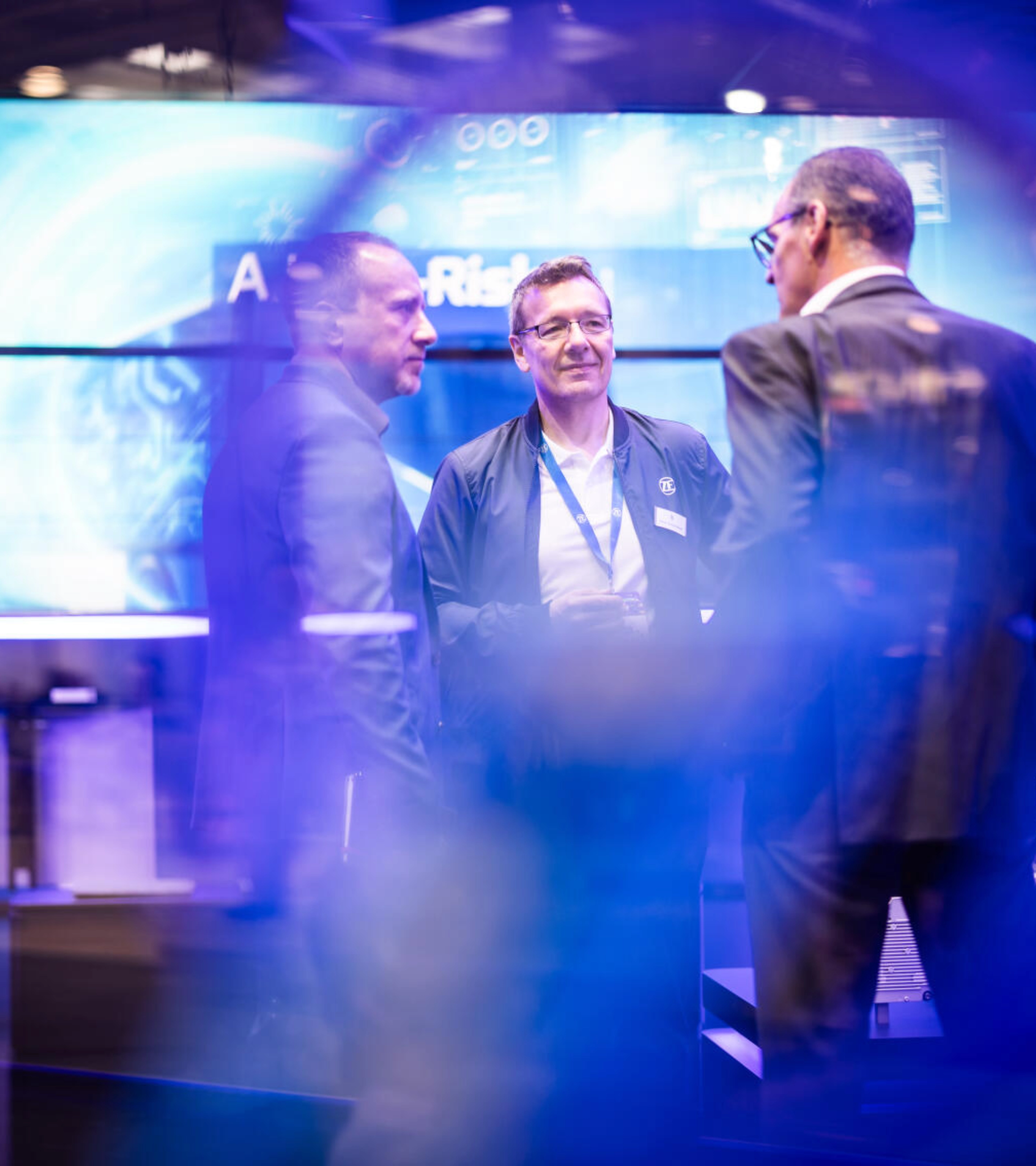 Drei Männer unterhalten sich an einem Messestand für Technologie.