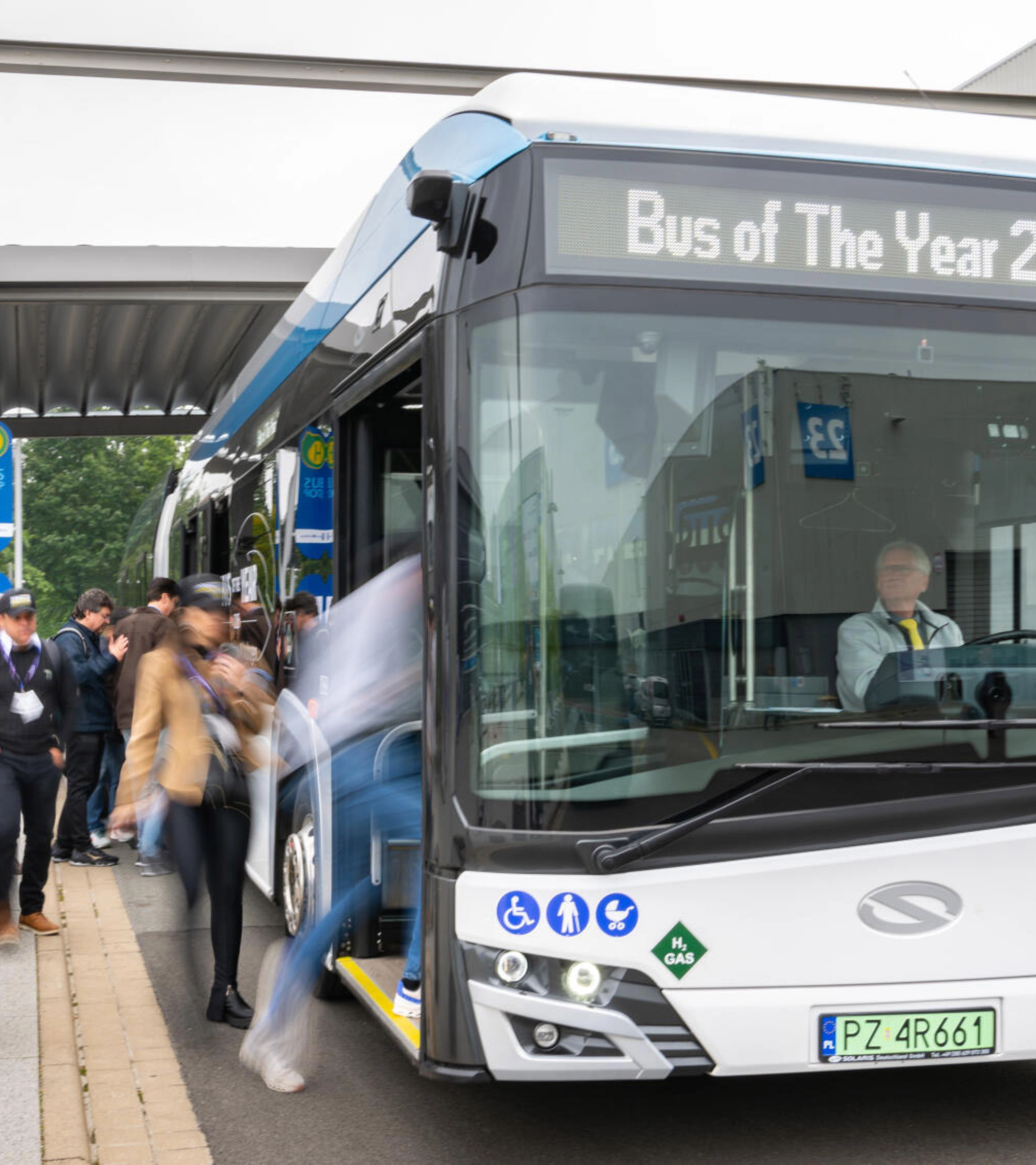 Hydrogen shuttle bus marked “Bus of The Year 2025” at a busy bus stop.