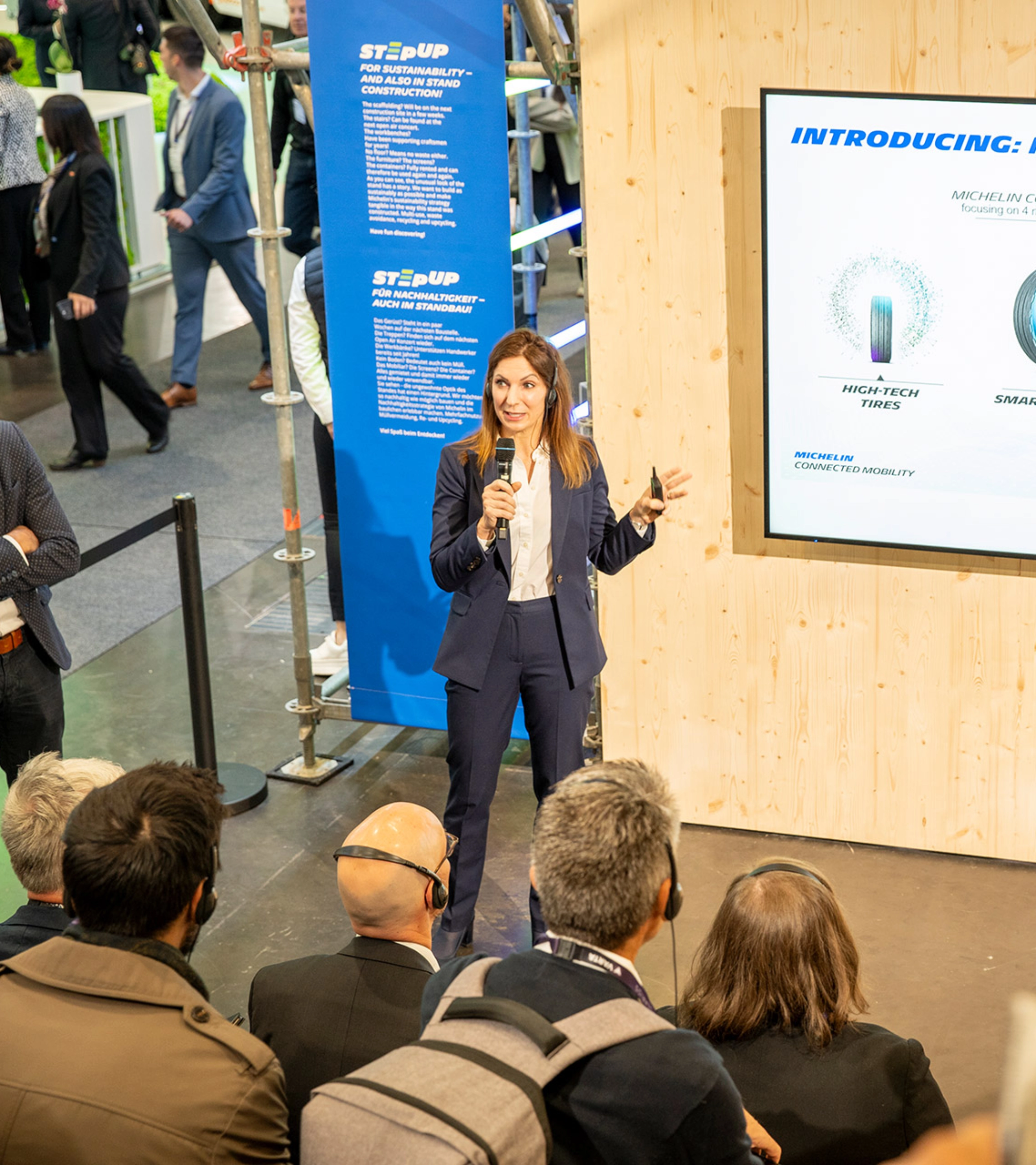 Woman presents Michelin Connected Mobility to audience at trade fair booth.
