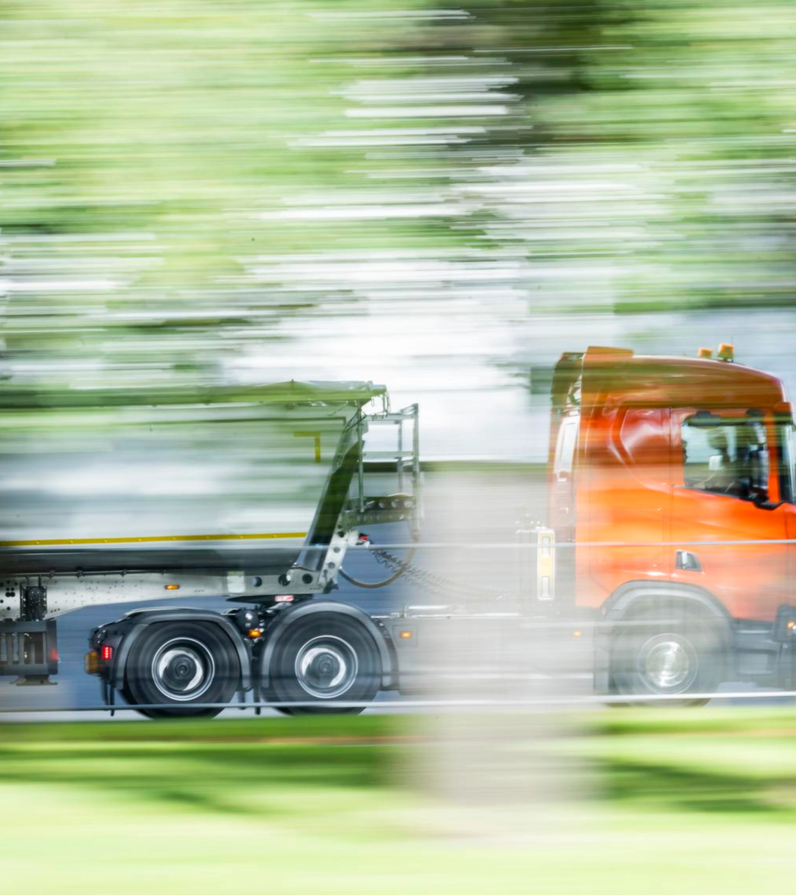 Ein Lkw mit Auflieger fährt auf einer von Grün umgebenen Straße.